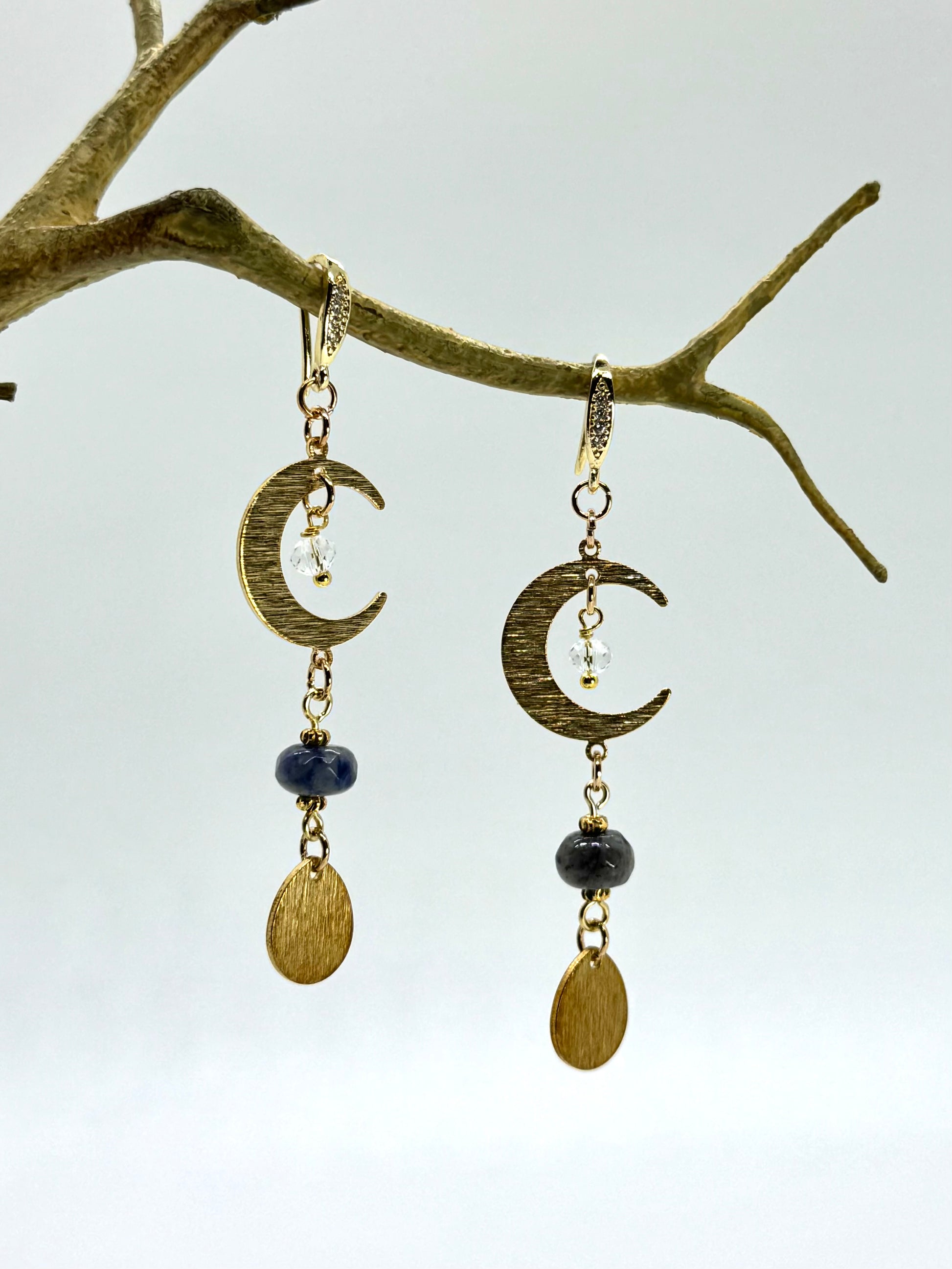 Gold crescent moon earrings with black beads hanging from a branch.