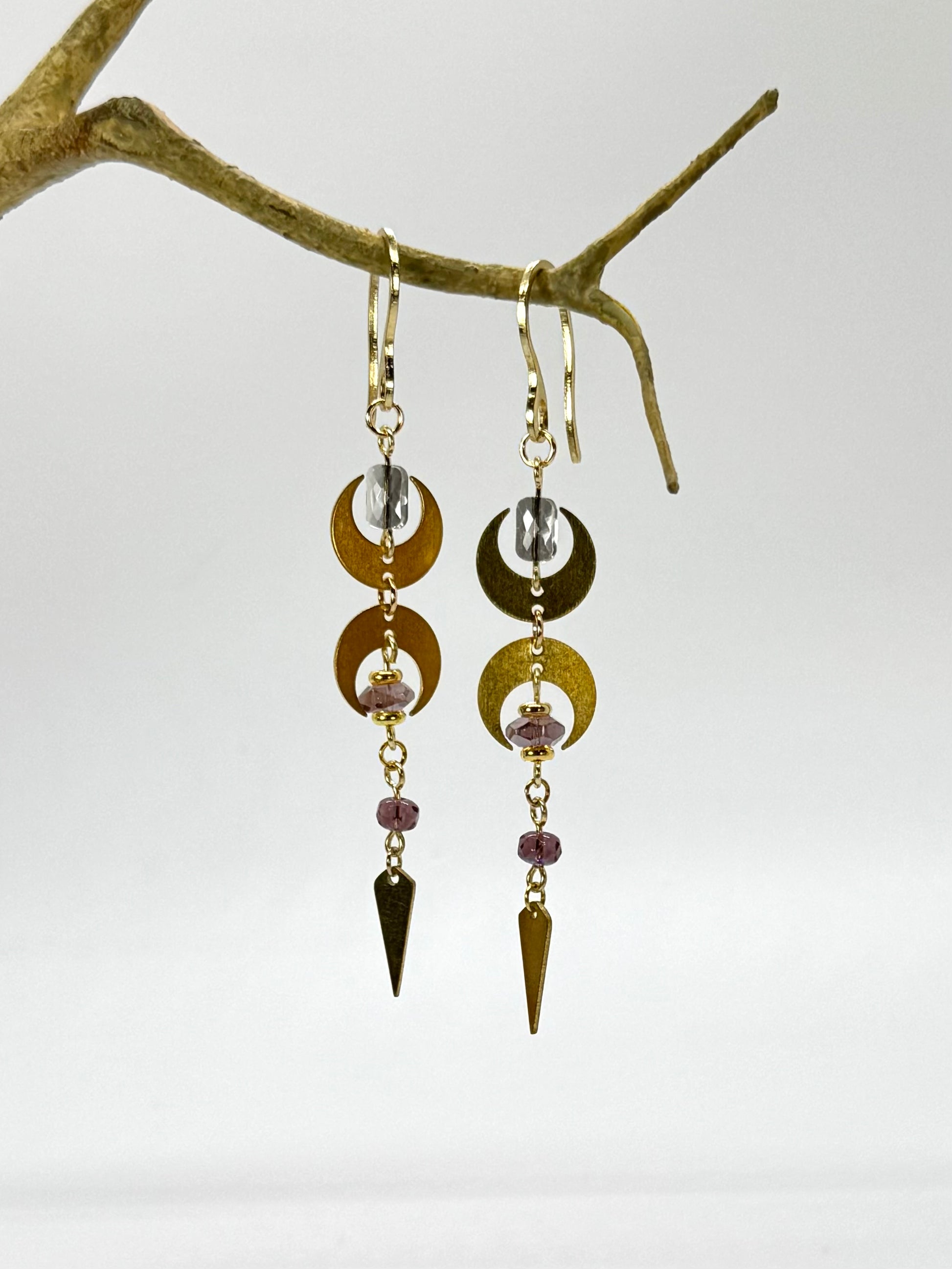 Gold and silver earrings with dangling elements on a branch against a white background