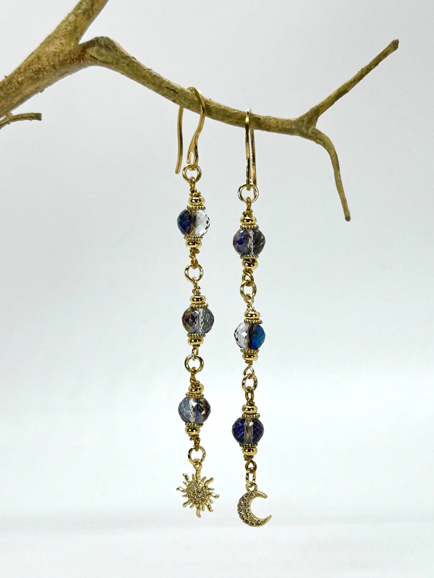 Pair of earrings with blue beads and gold accents hanging on a branch.