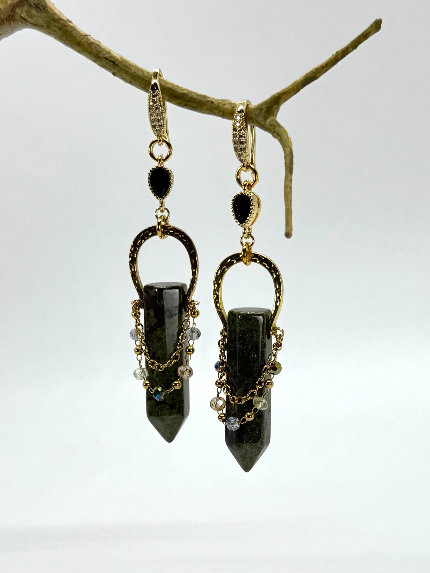 Pair of black stone earrings hanging from a branch on a white background