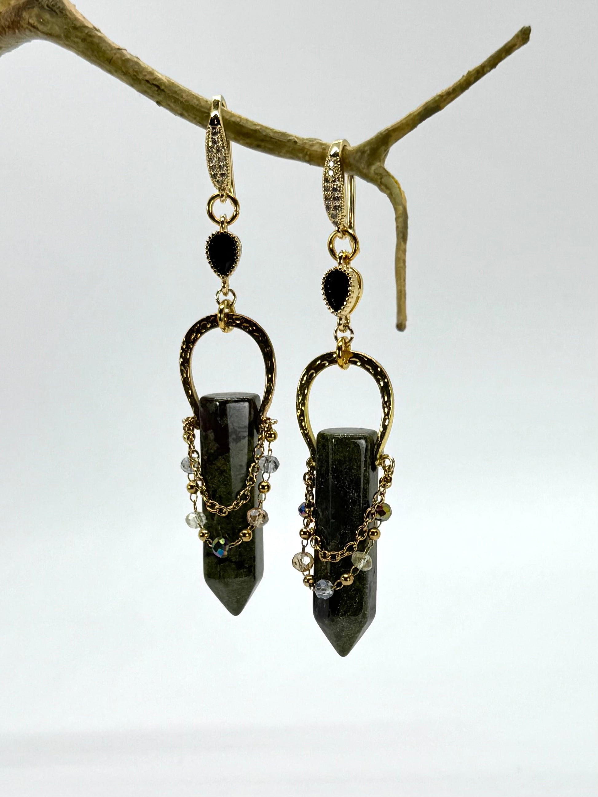 Pair of black stone earrings hanging from a branch on a white background