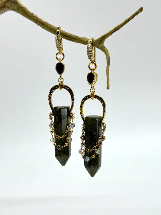 Pair of black stone earrings hanging from a branch on a white background