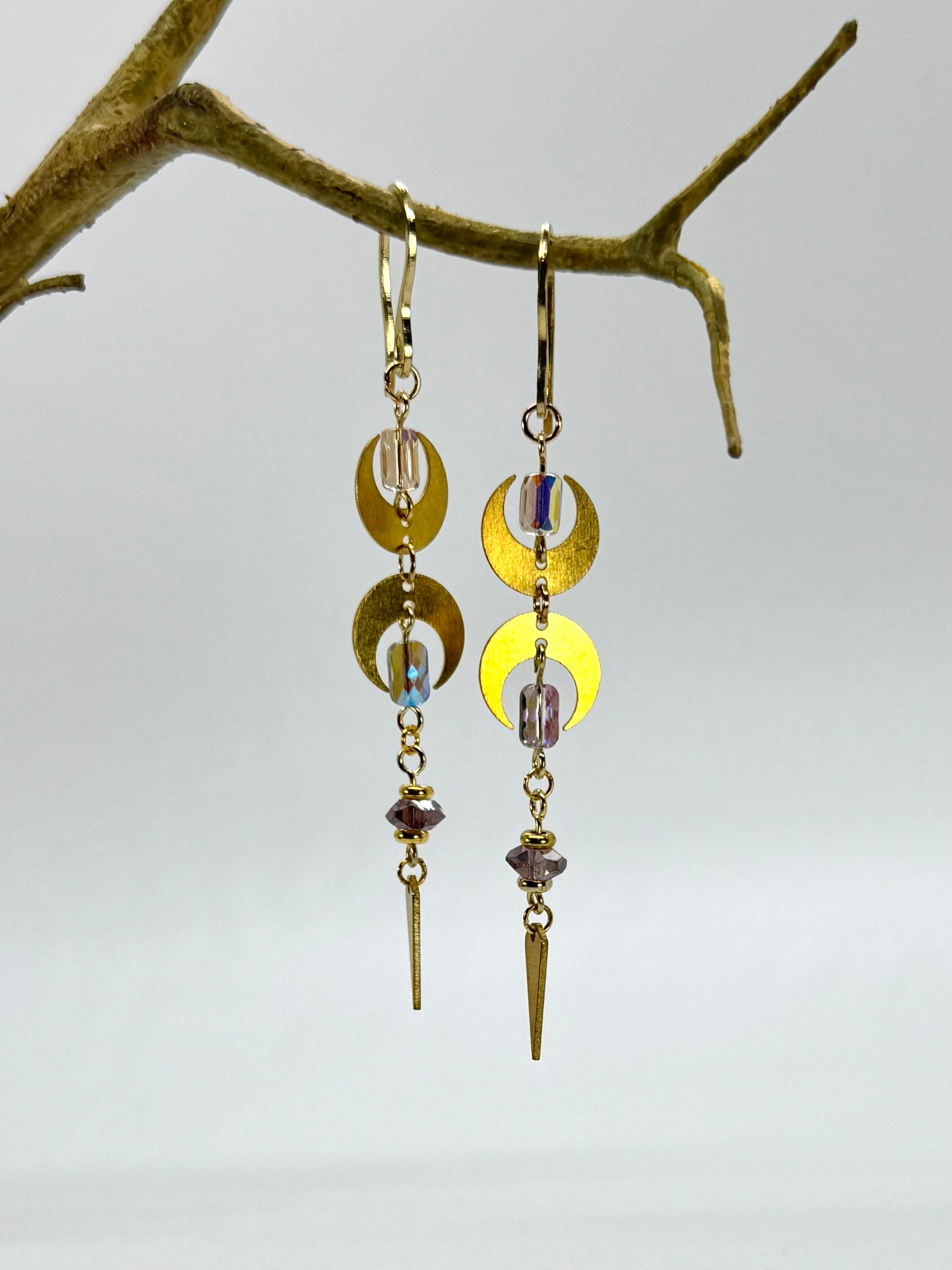 Pair of gold and yellow dangling earrings on a branch against a light gray background