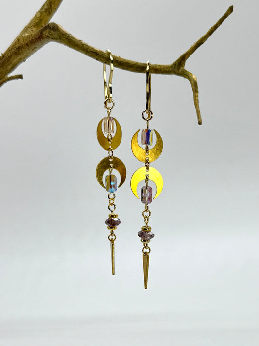 Pair of gold and yellow dangling earrings on a branch against a light gray background
