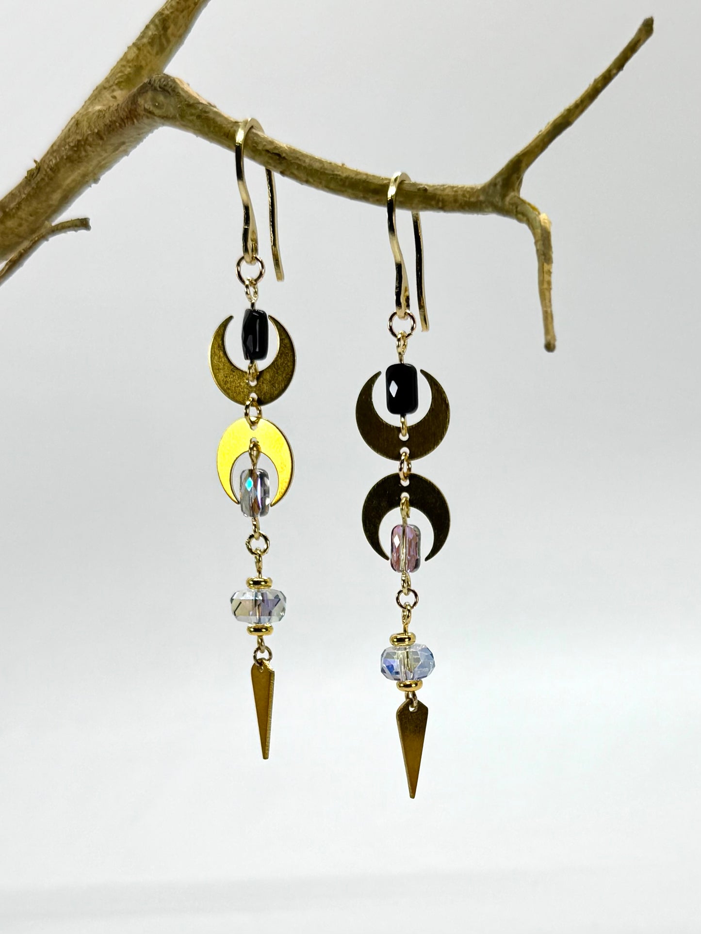 Pair of earrings with geometric designs hanging on a branch against a white background