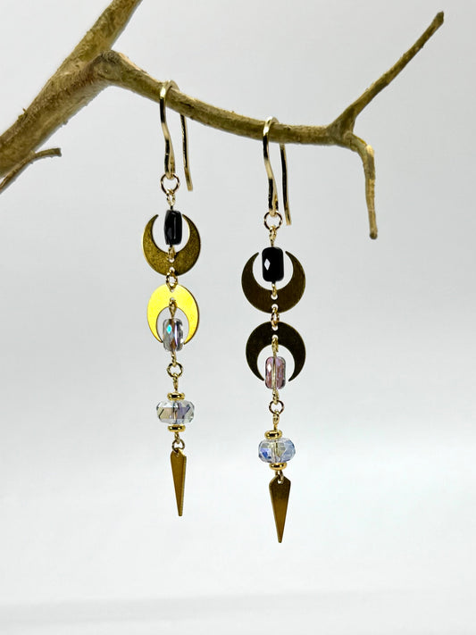 Pair of earrings with geometric designs hanging on a branch against a white background