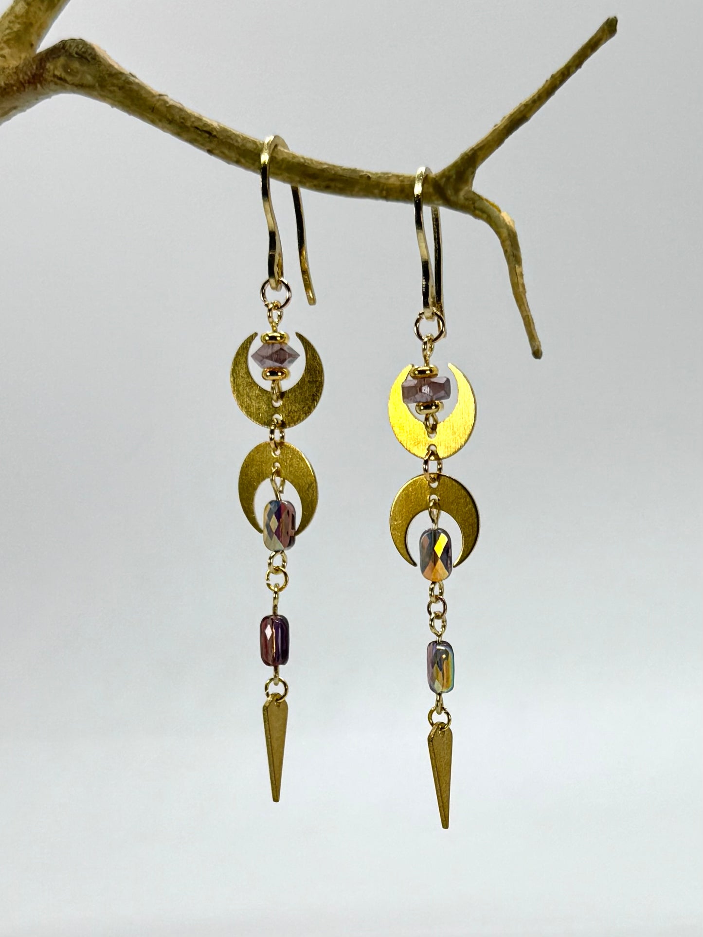 Gold and bronze earrings with gemstones hanging from a branch against a light background