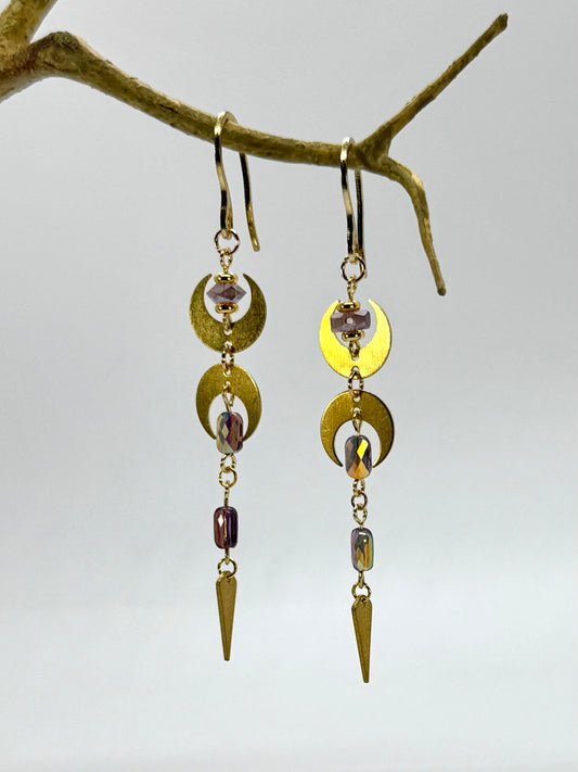 Gold and bronze earrings with gemstones hanging from a branch against a light background