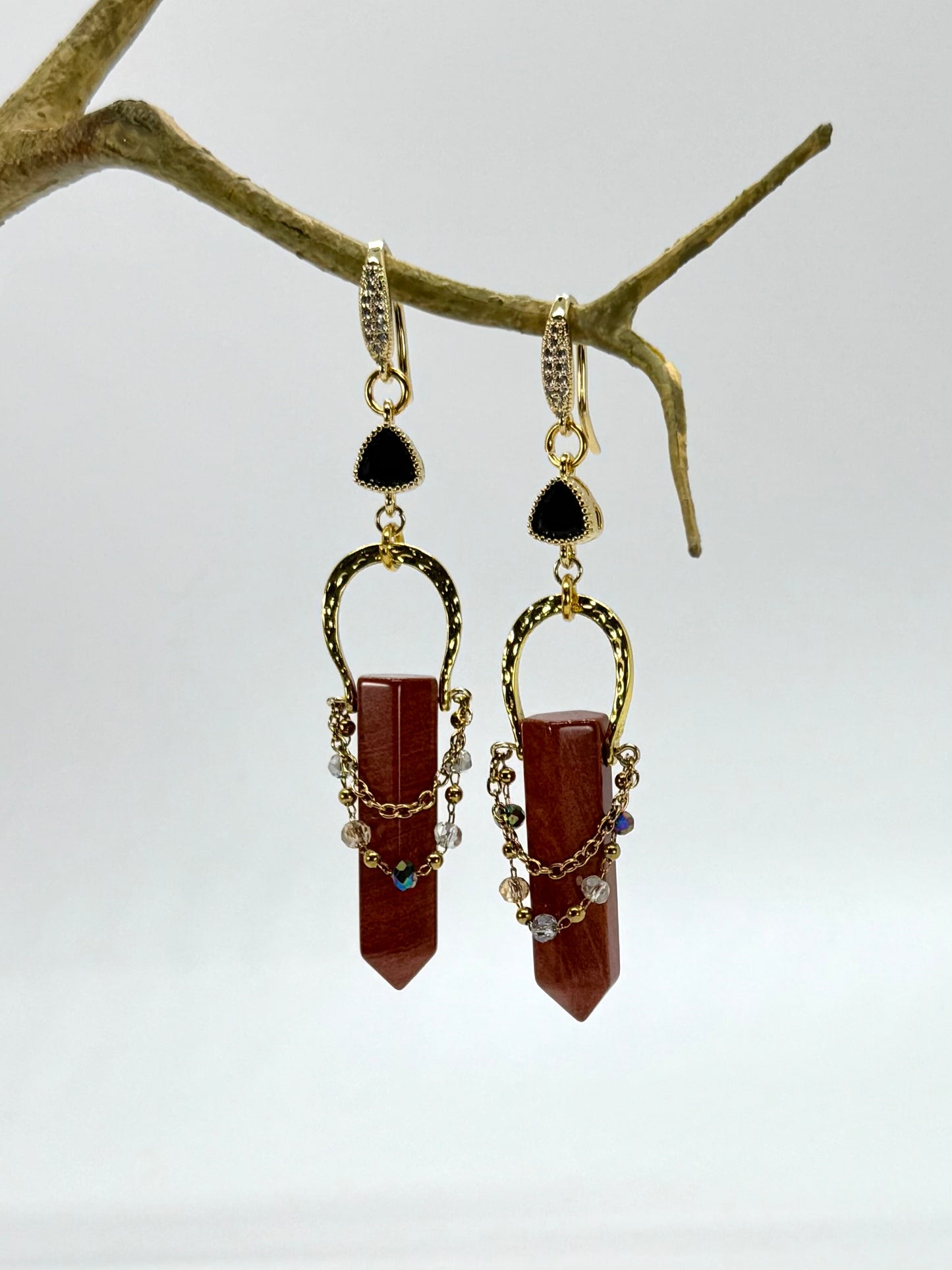 Pair of gold and brown earrings on a branch against a white background