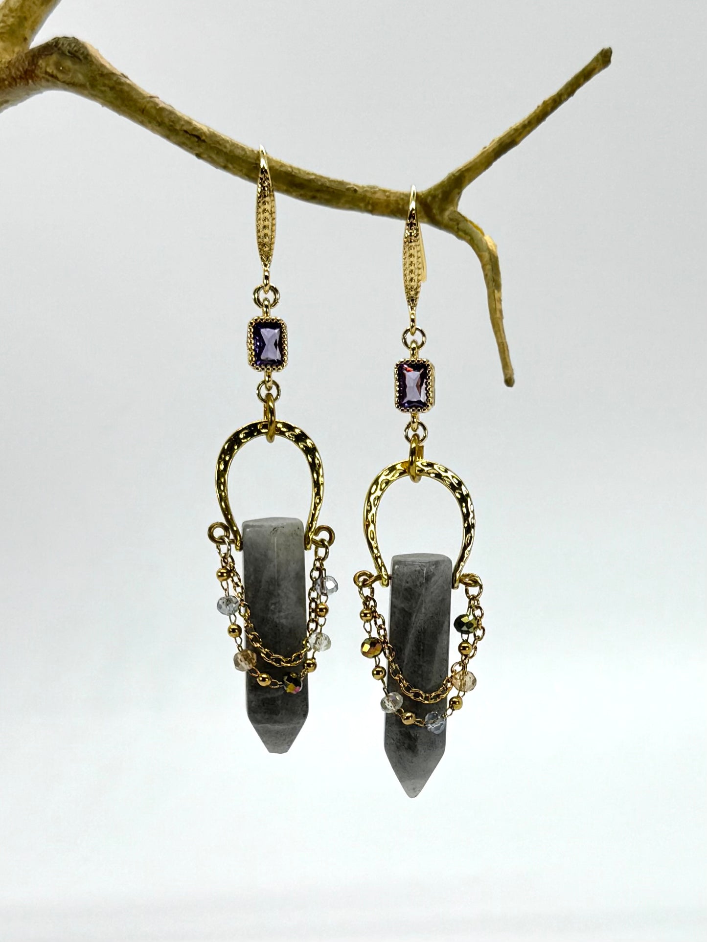 Pair of gold and black earrings hanging from a branch against a white background
