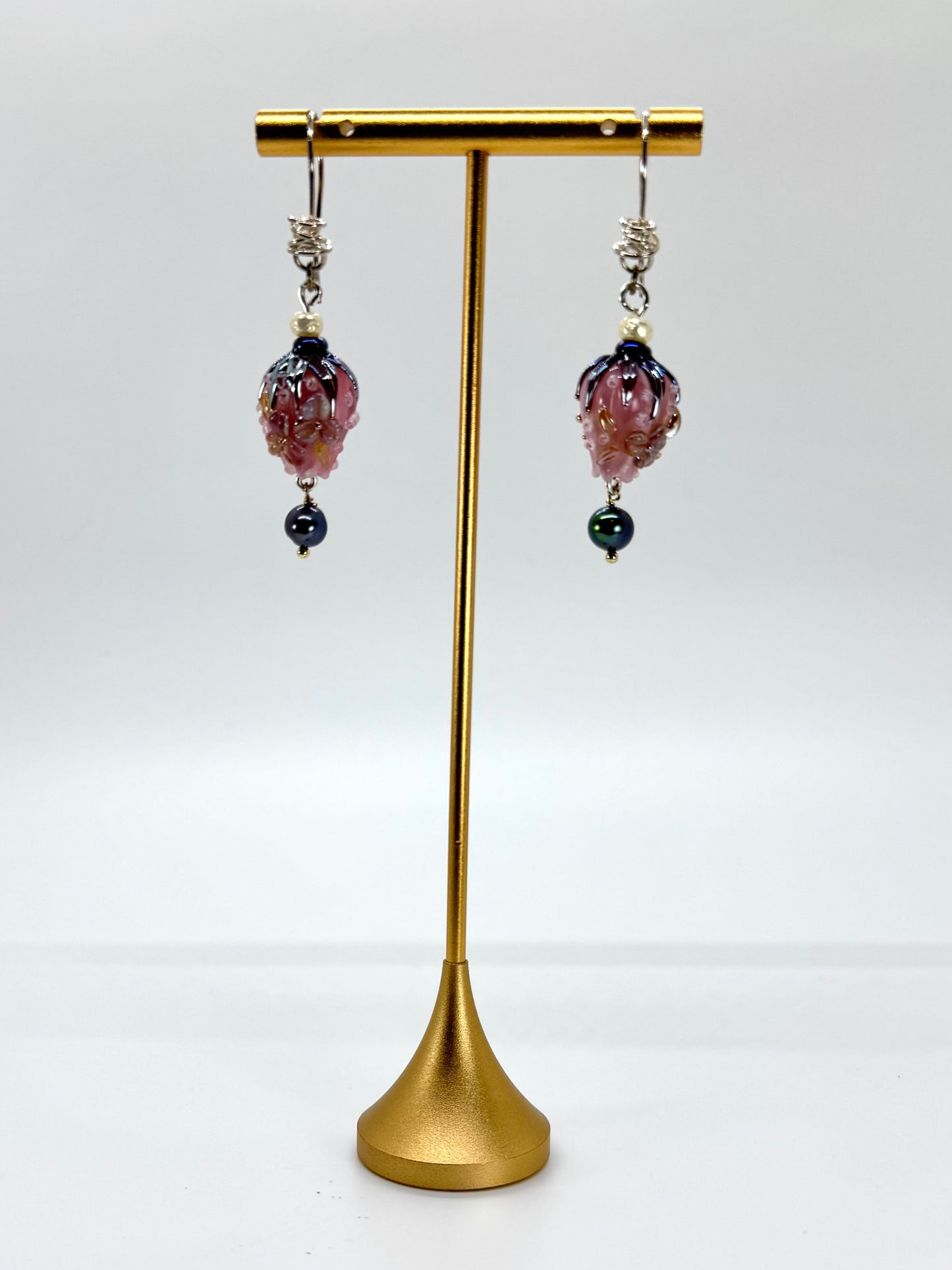 Pair of earrings with purple and black beads on a gold stand against a white background