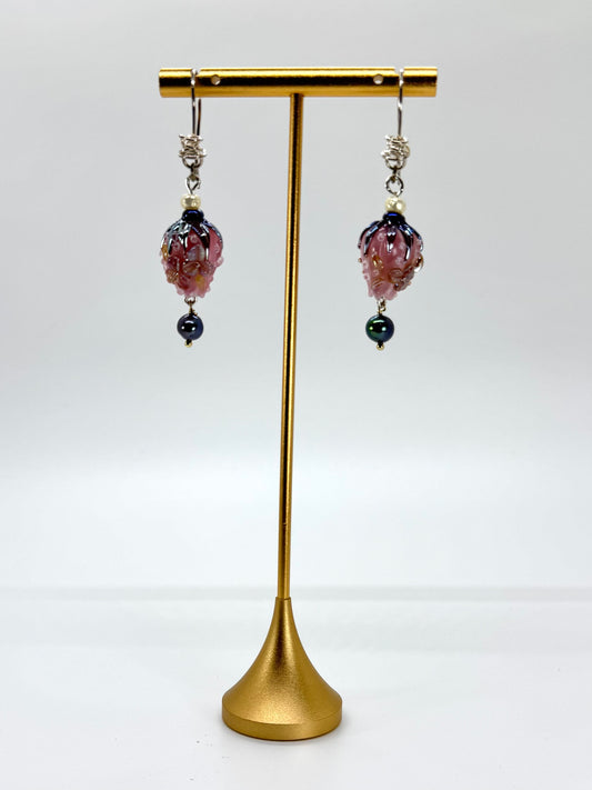 Pair of earrings with purple and black beads on a gold stand against a white background
