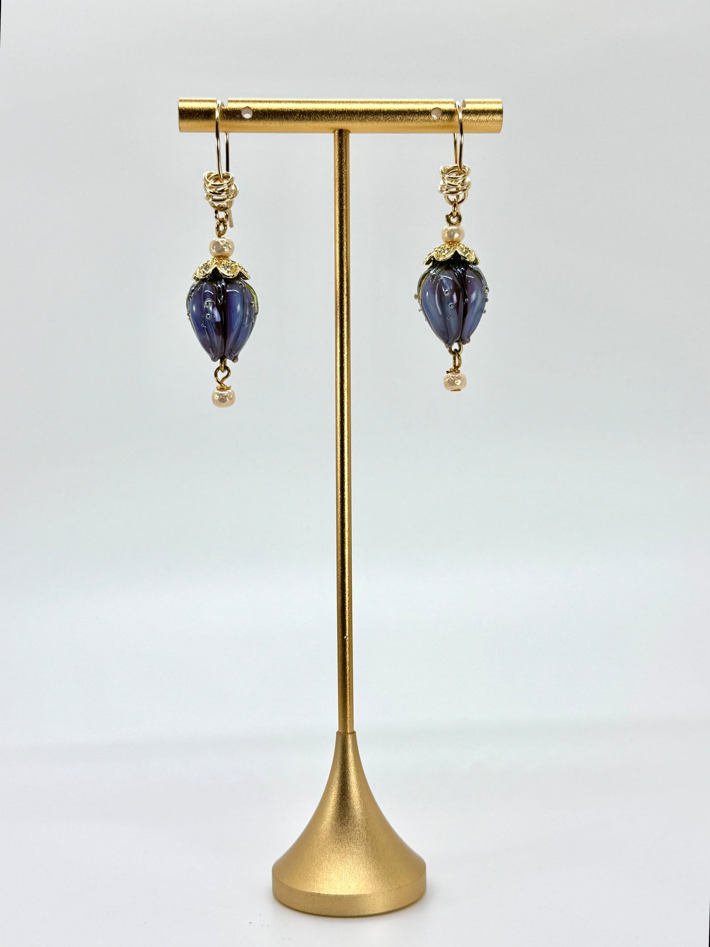 Pair of purple earrings on a gold stand against a white background