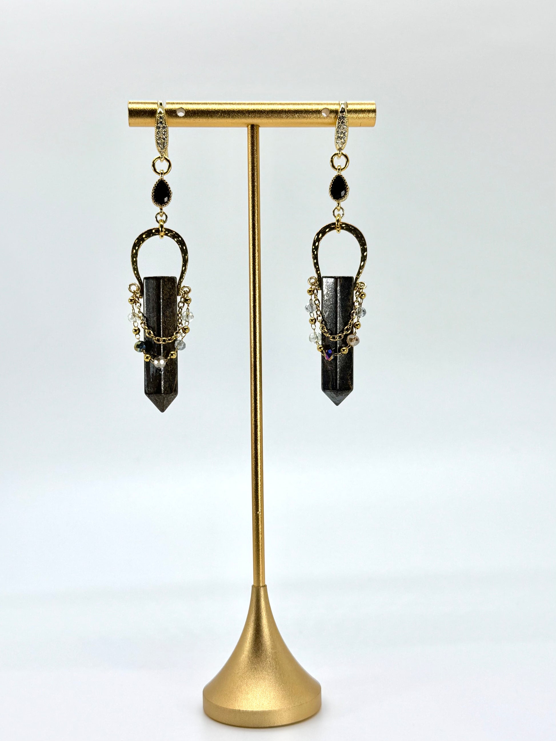 Pair of black crystal earrings on a gold stand against a white background