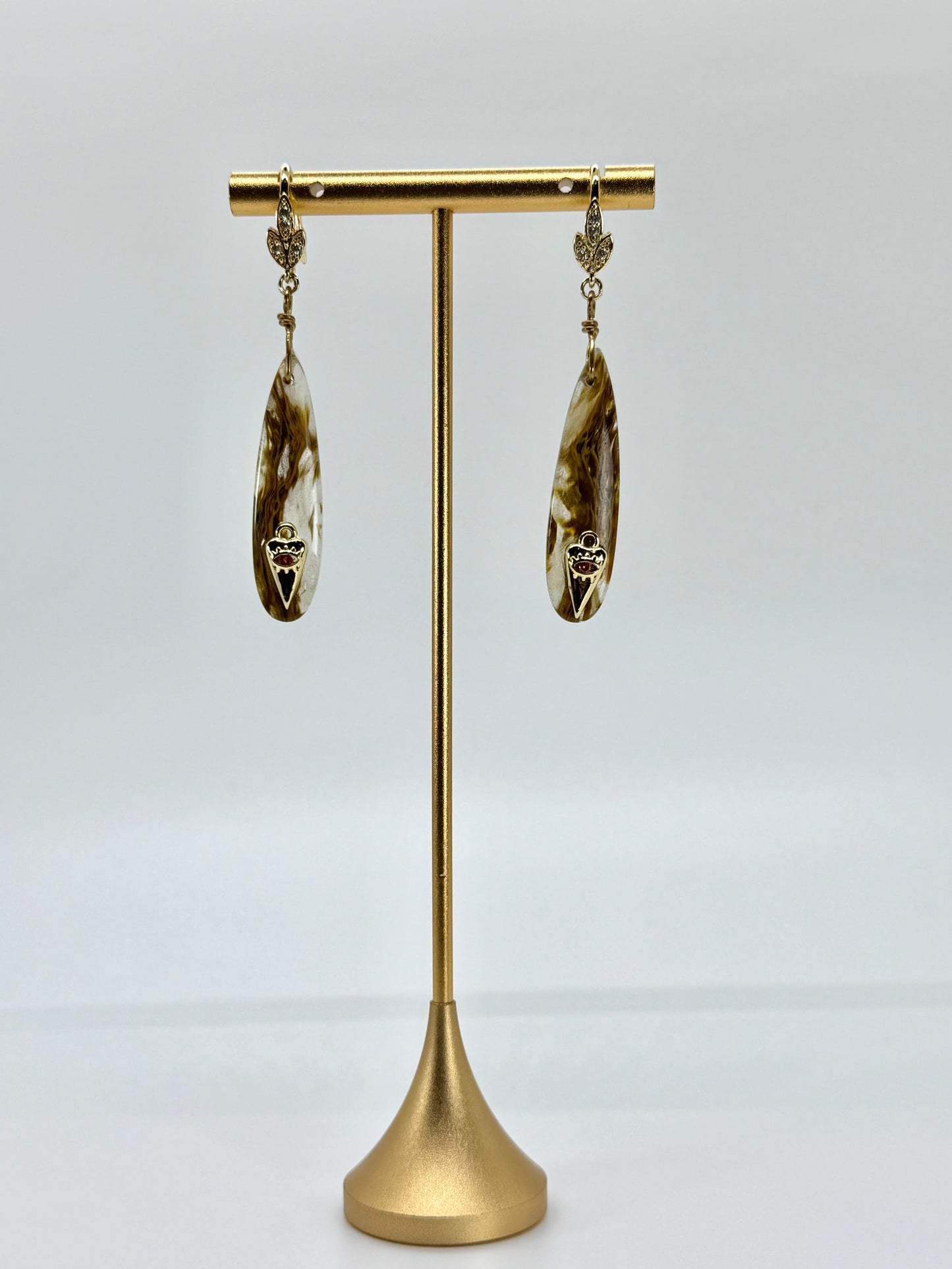 Pair of gold earrings on a gold stand against a white background