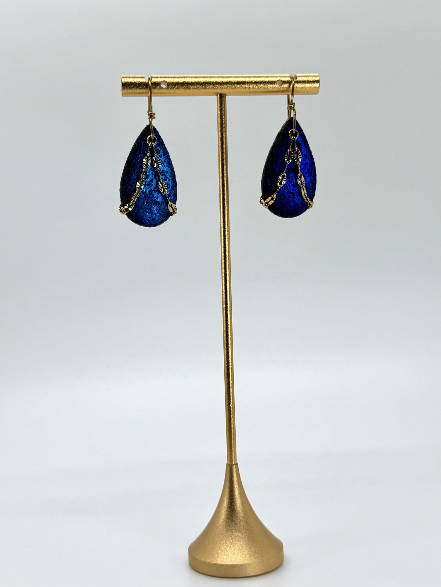 Blue teardrop earrings on a gold stand against a white background