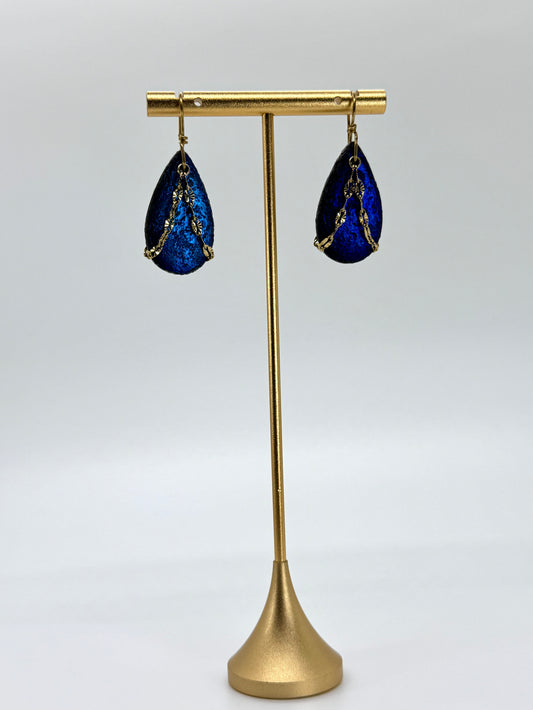Blue teardrop earrings on a gold stand against a white background