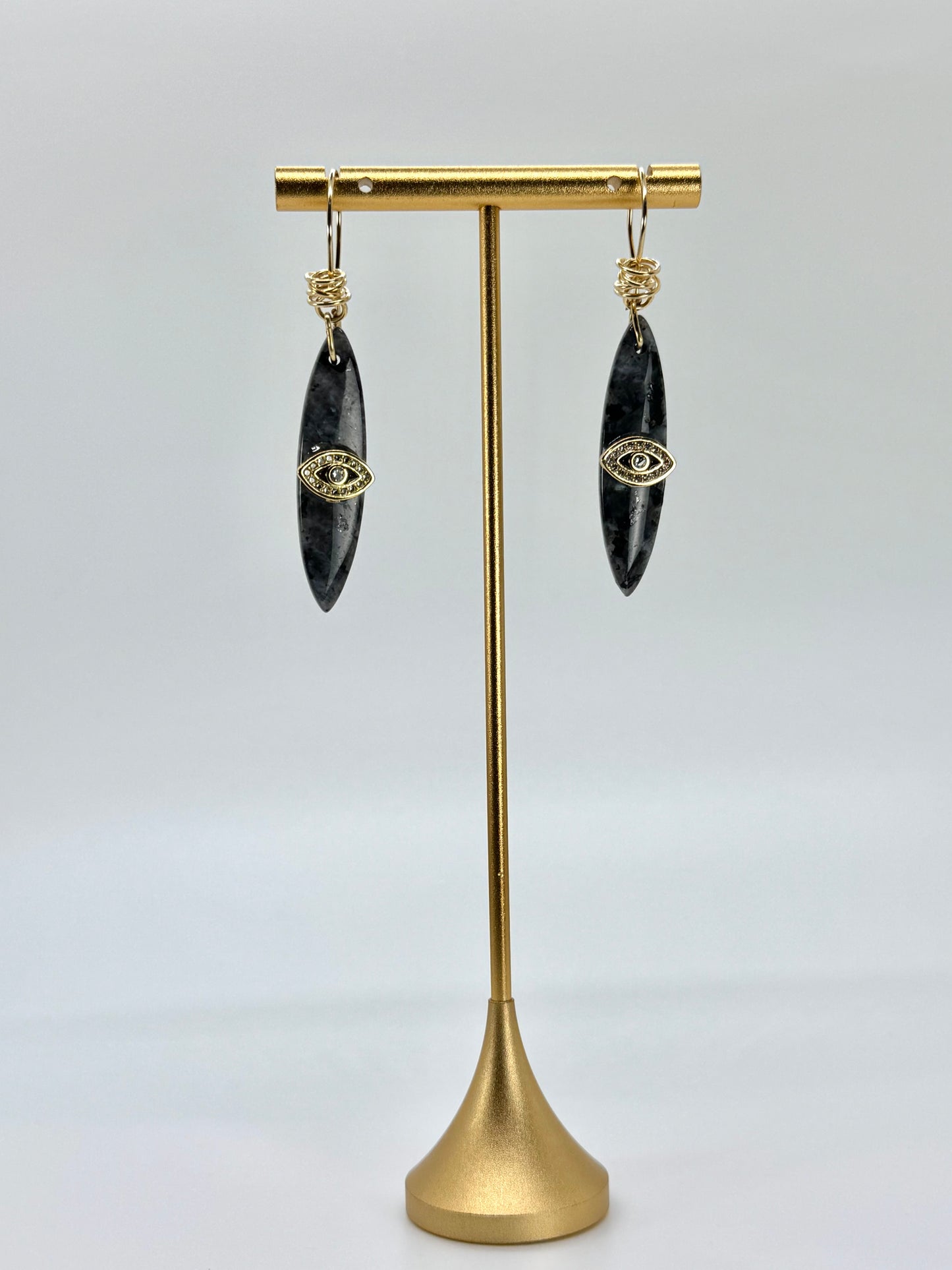 Black earrings with gold accents on a gold stand against a light gray background