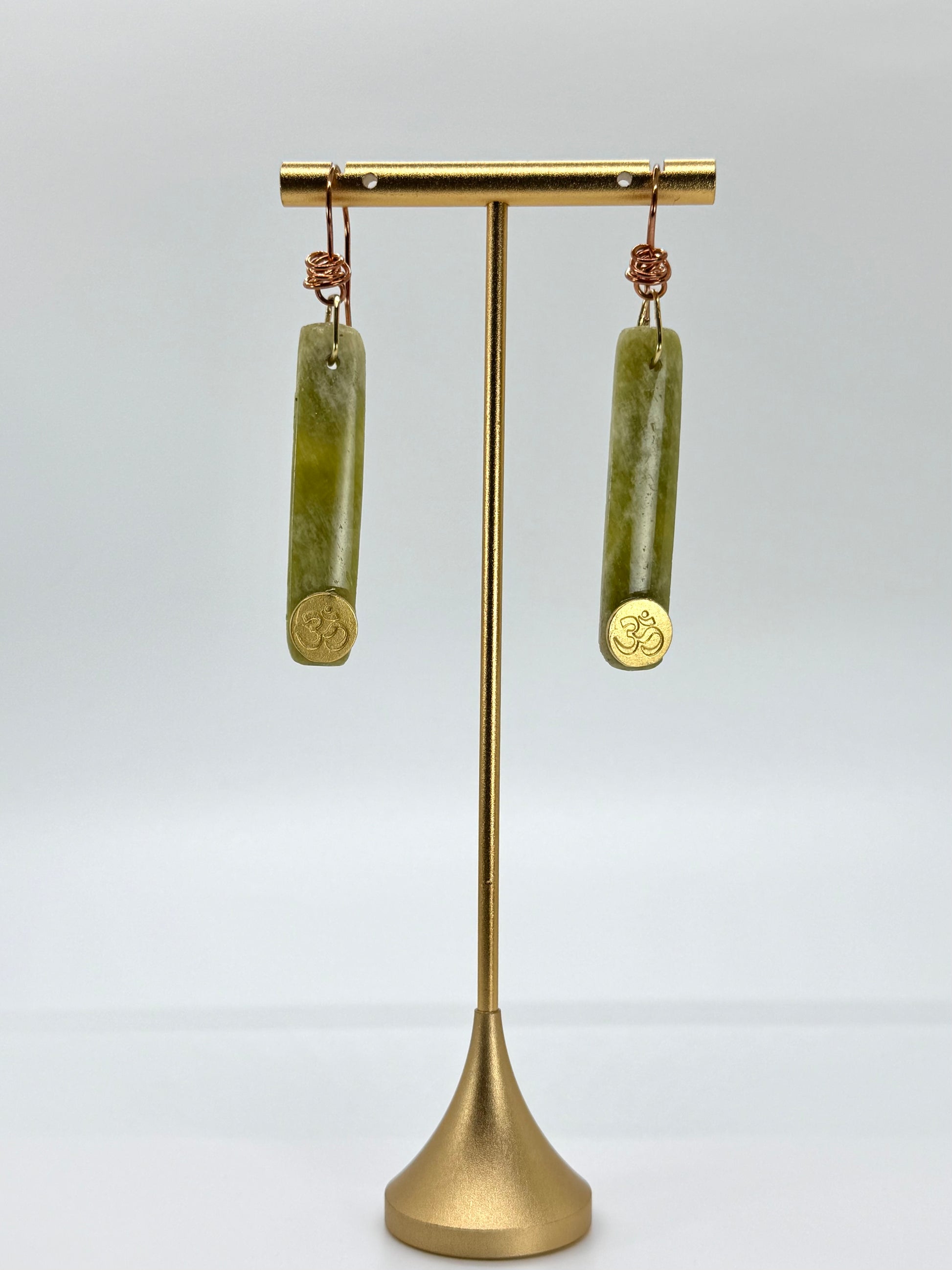 Gold earring stand with green cylindrical earrings on a white background