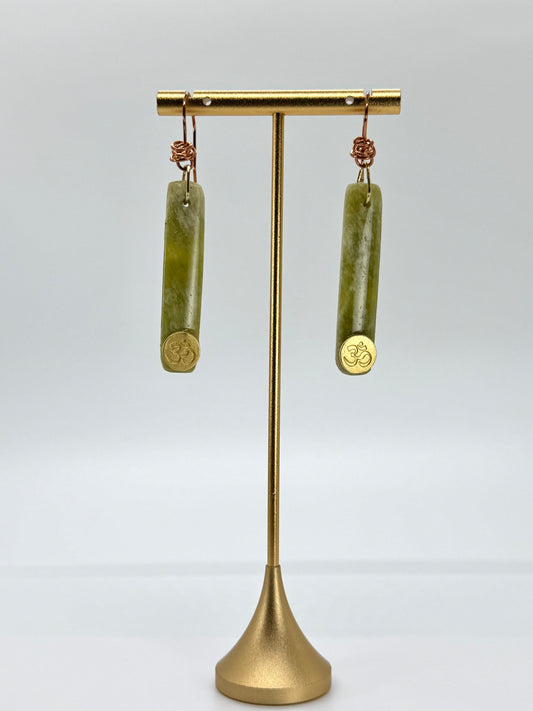 Gold earring stand with green cylindrical earrings on a white background