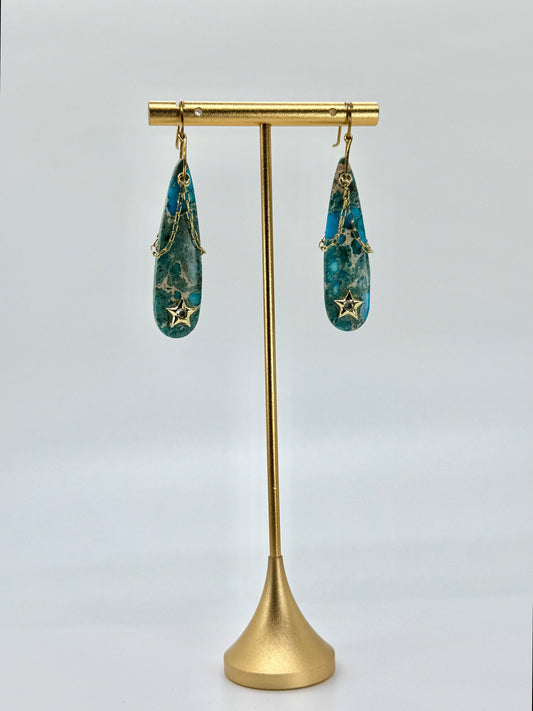 Gold earring stand with blue earrings on a white background