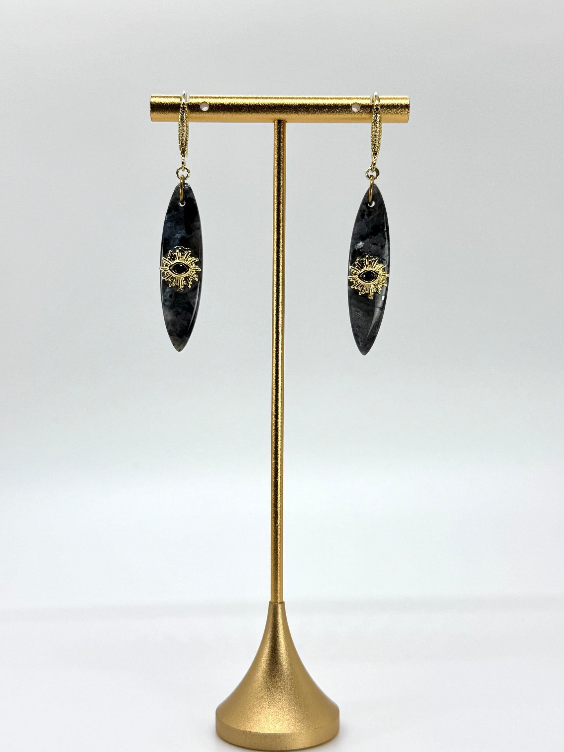Pair of black earrings with gold accents on a brass stand against a white background
