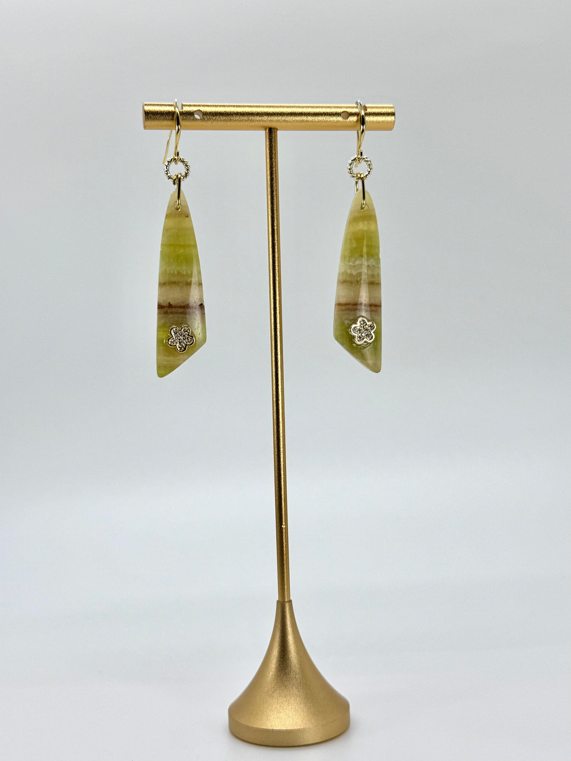 Green leaf-shaped earrings on a gold stand against a white background