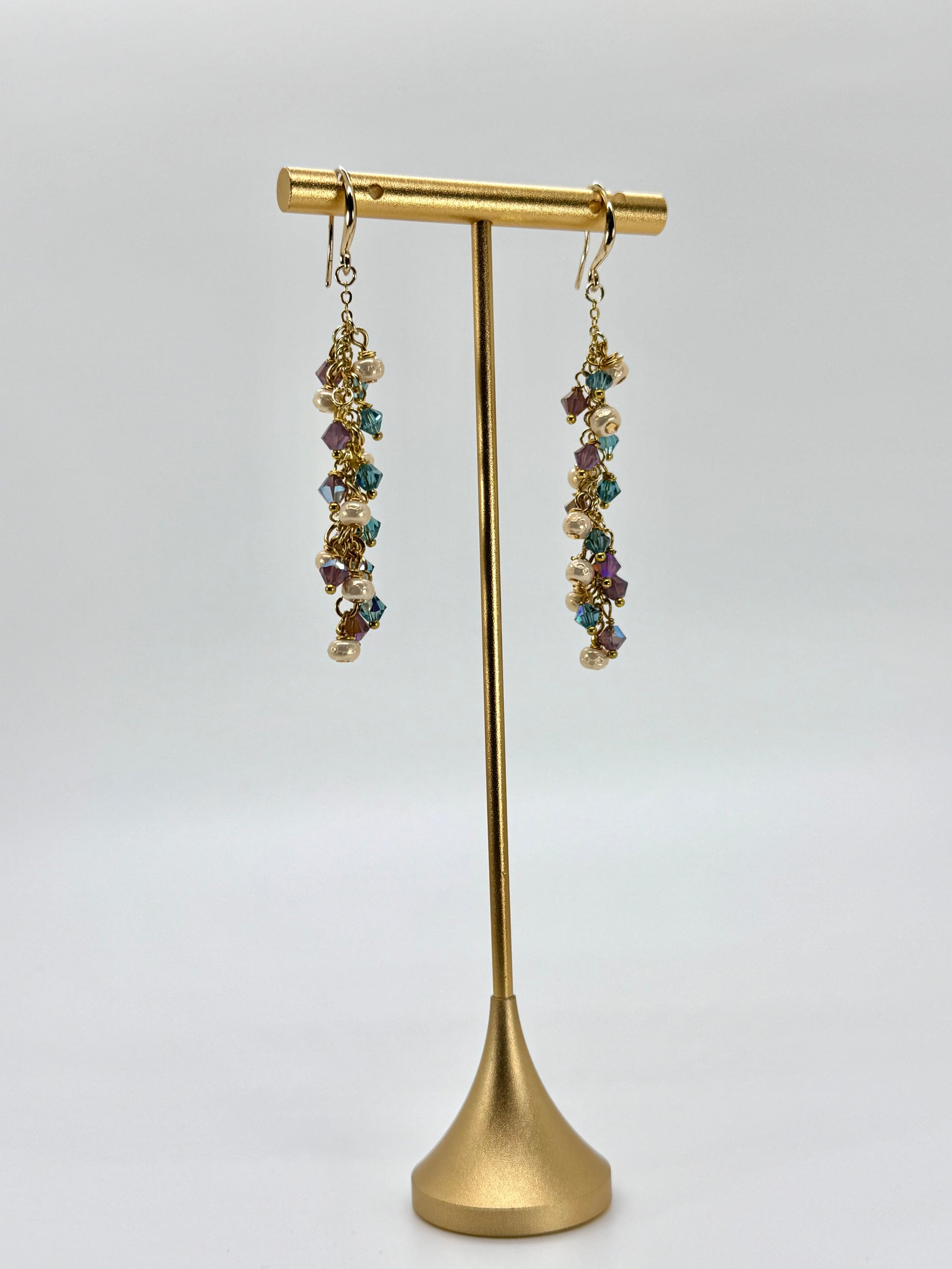 Gold earring stand with multicolored gemstone earrings on a white background