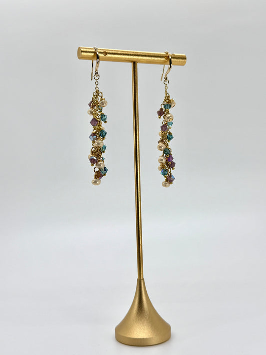 Gold earring stand with multicolored gemstone earrings on a white background