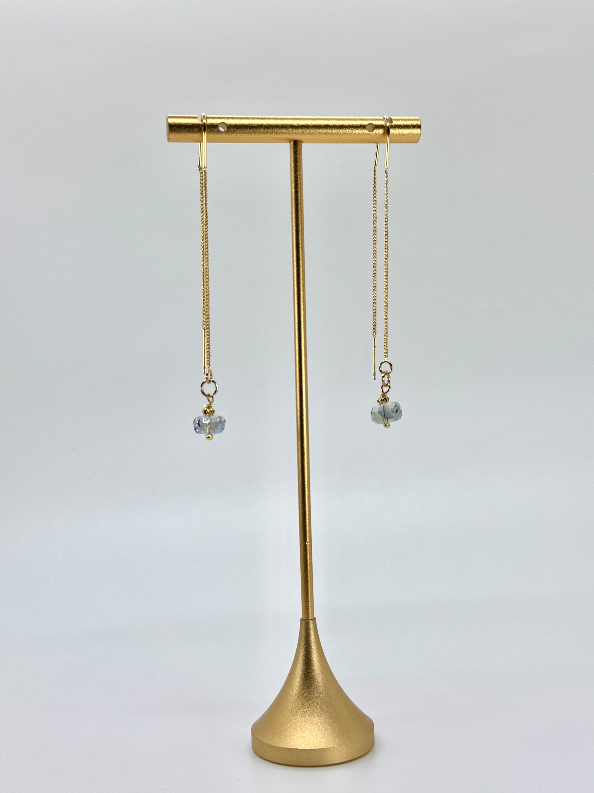 Gold earring stand with two dangling earrings on a light gray background