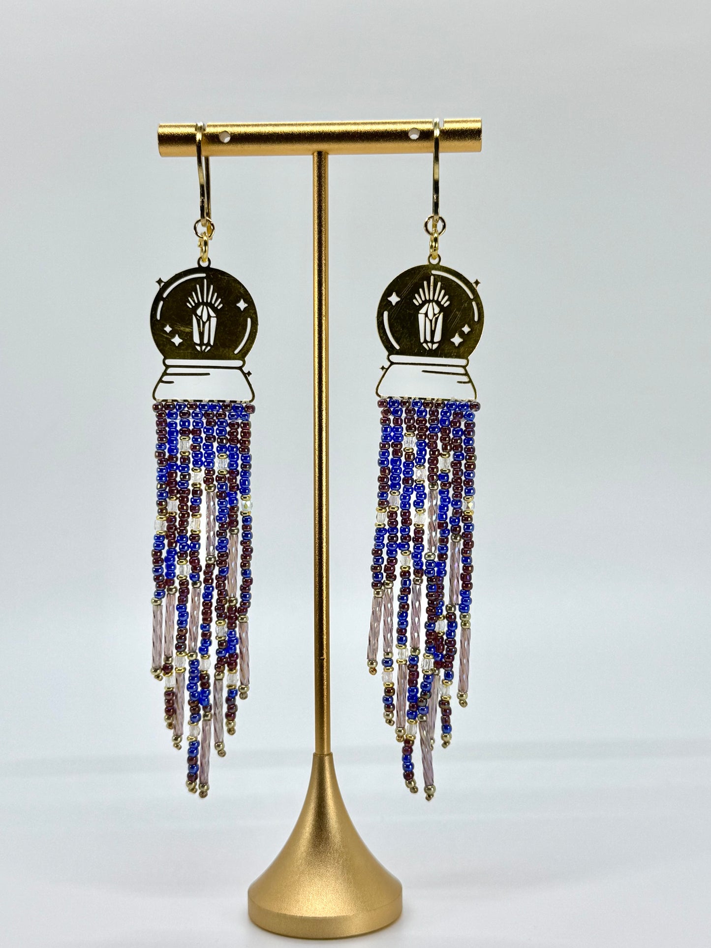 Beaded earrings on a gold stand against a gray background
