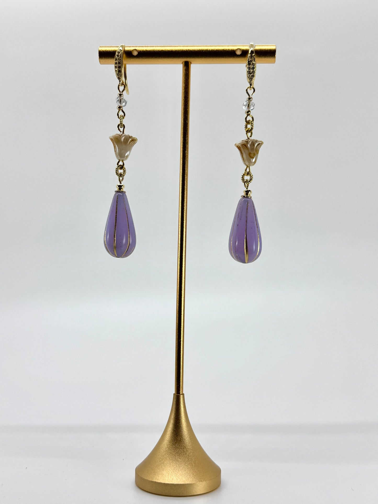 Purple teardrop earrings on a gold stand against a white background