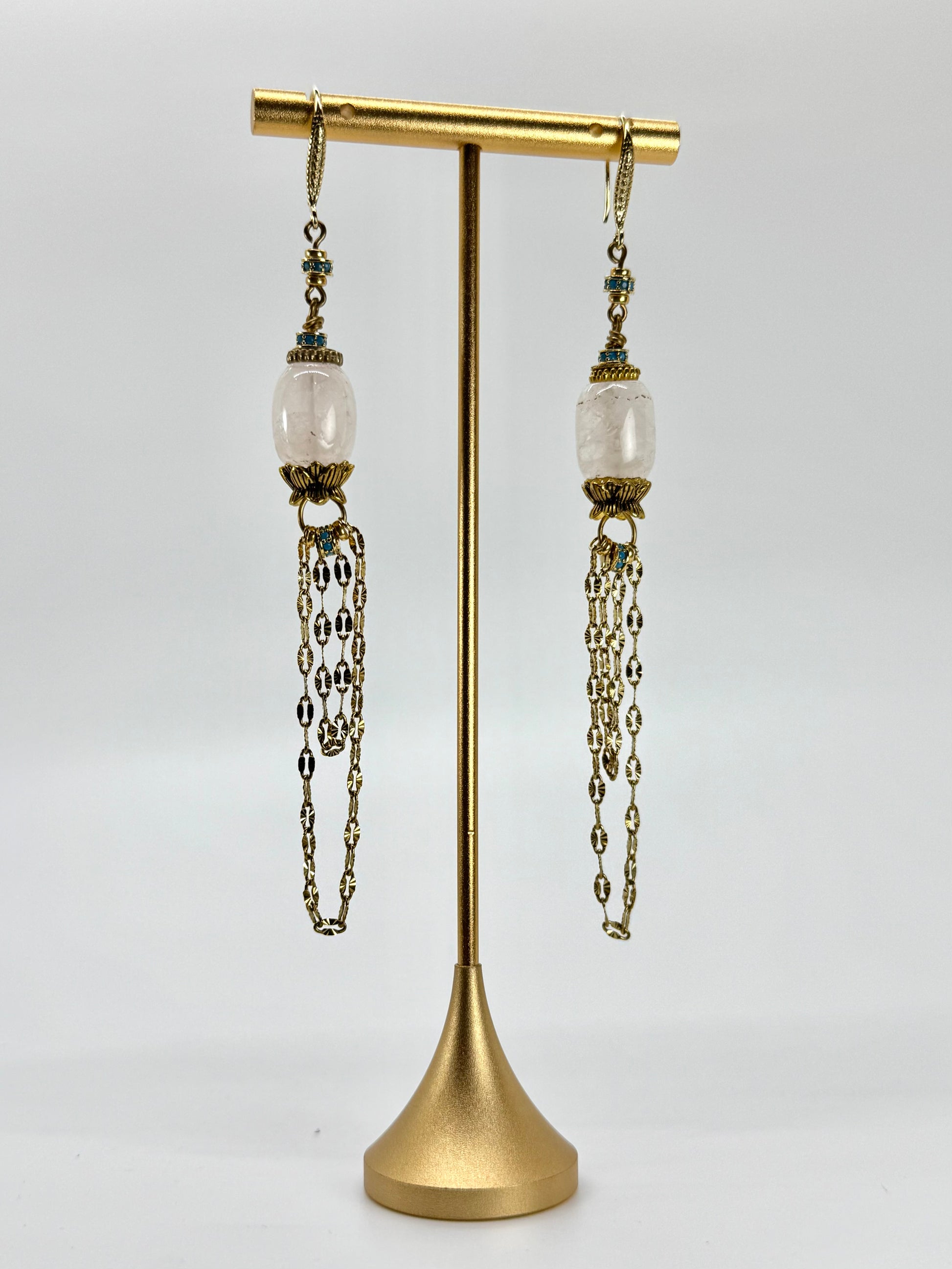 Pair of earrings with chains on a gold stand against a white background