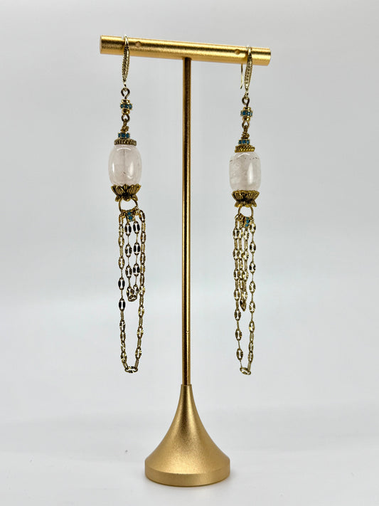 Pair of earrings with chains on a gold stand against a white background