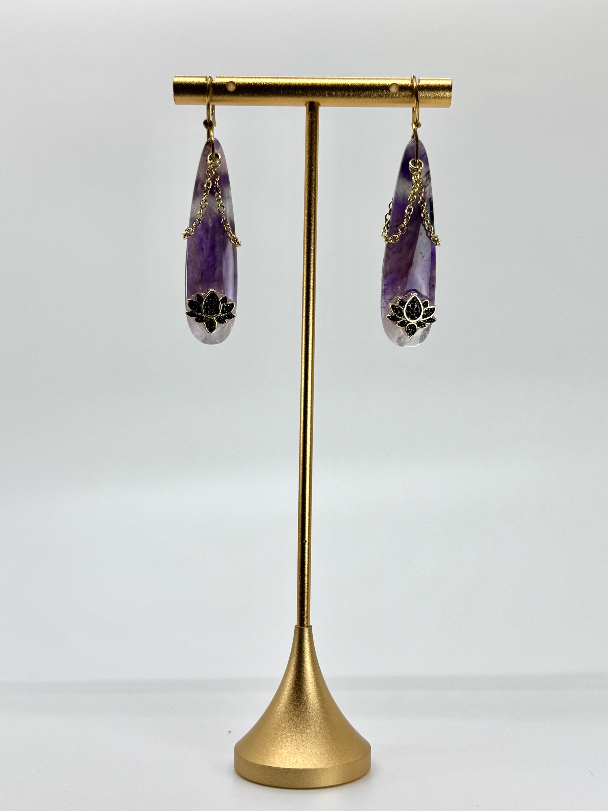 Purple teardrop earrings on a gold stand against a white background