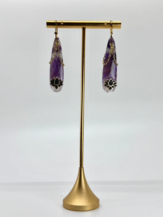 Purple teardrop earrings on a gold stand against a white background