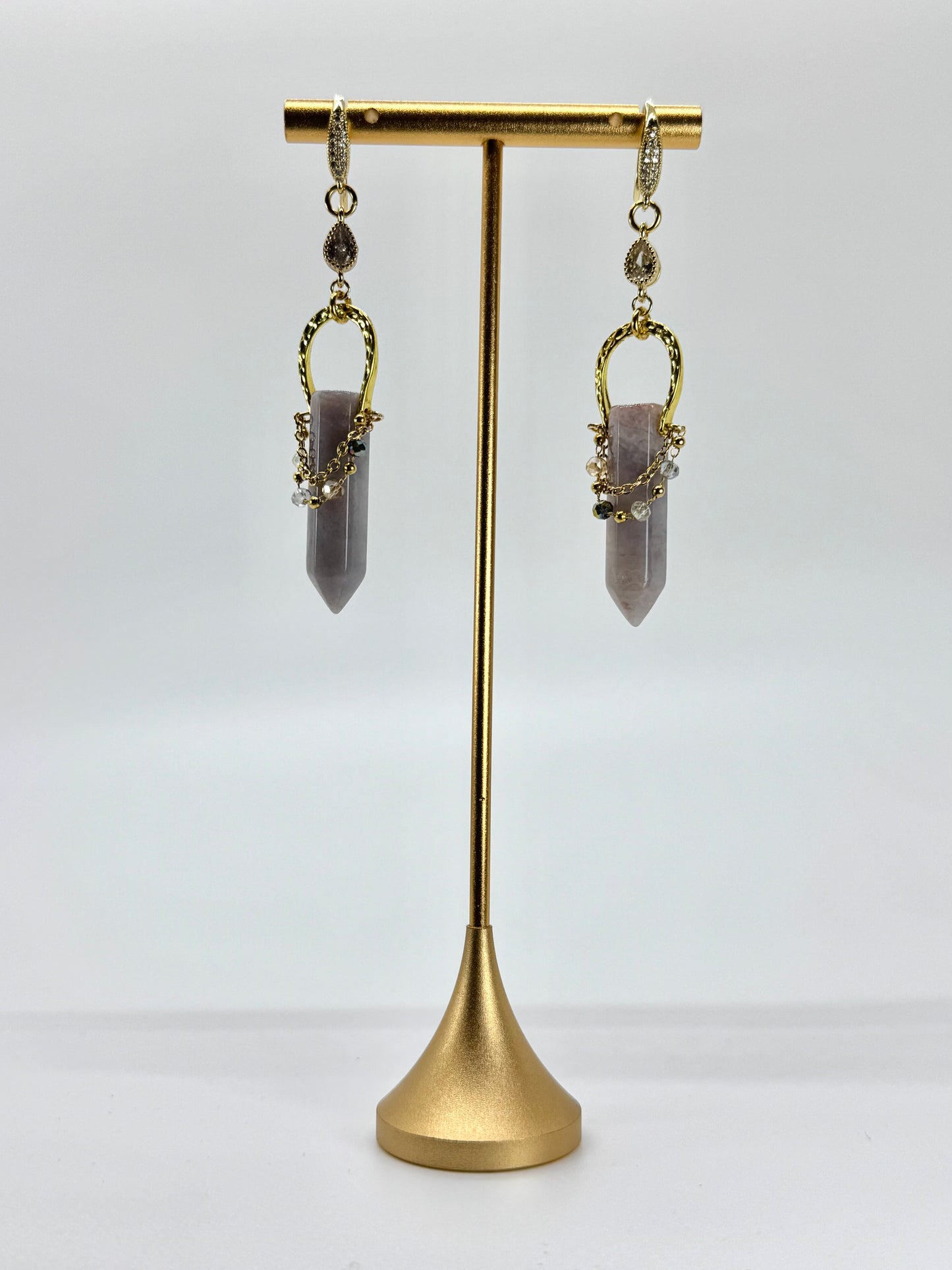 Gold earrings with purple gemstones on a gold stand against a white background