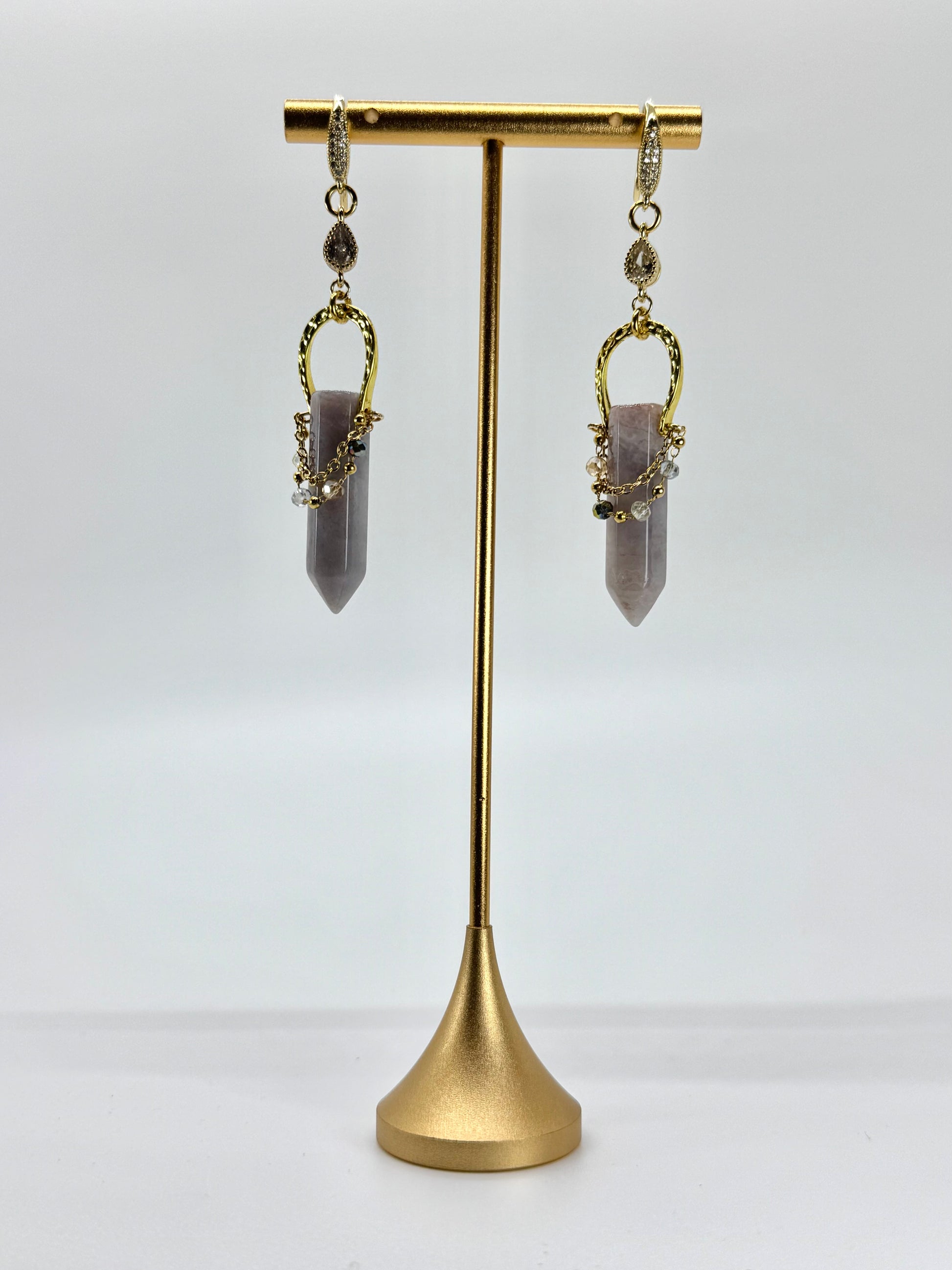 Gold earrings with purple gemstones on a gold stand against a white background