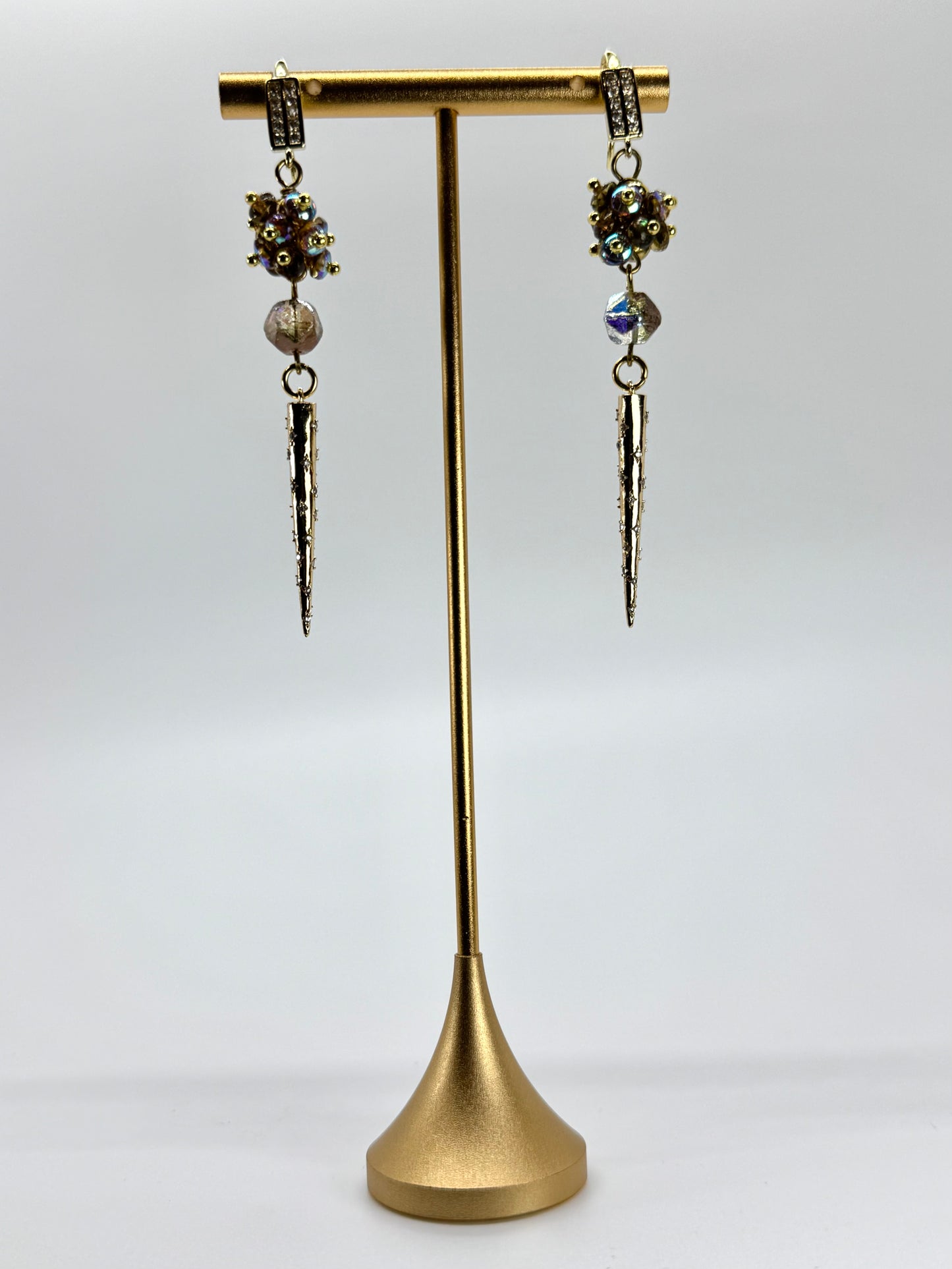 Pair of dangling earrings on a gold stand against a white background