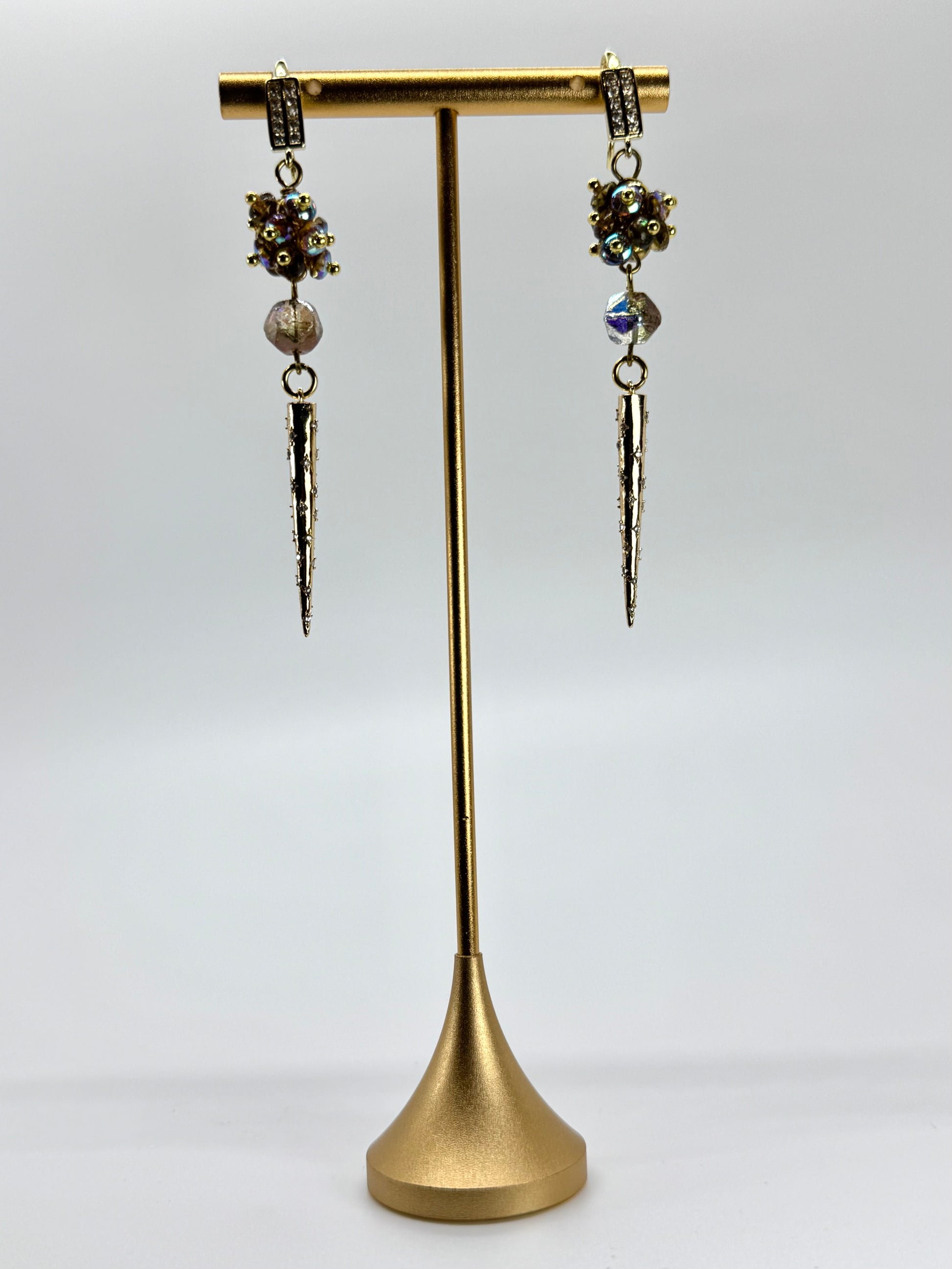 Pair of dangling earrings on a gold stand against a white background