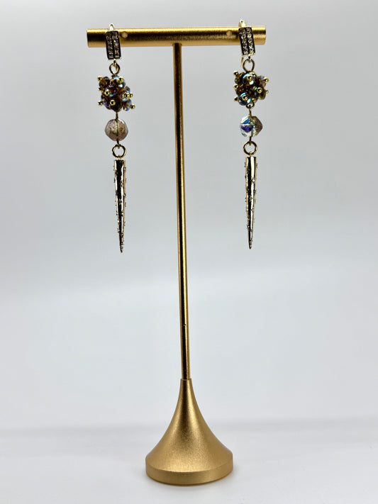 Pair of dangling earrings on a gold stand against a white background