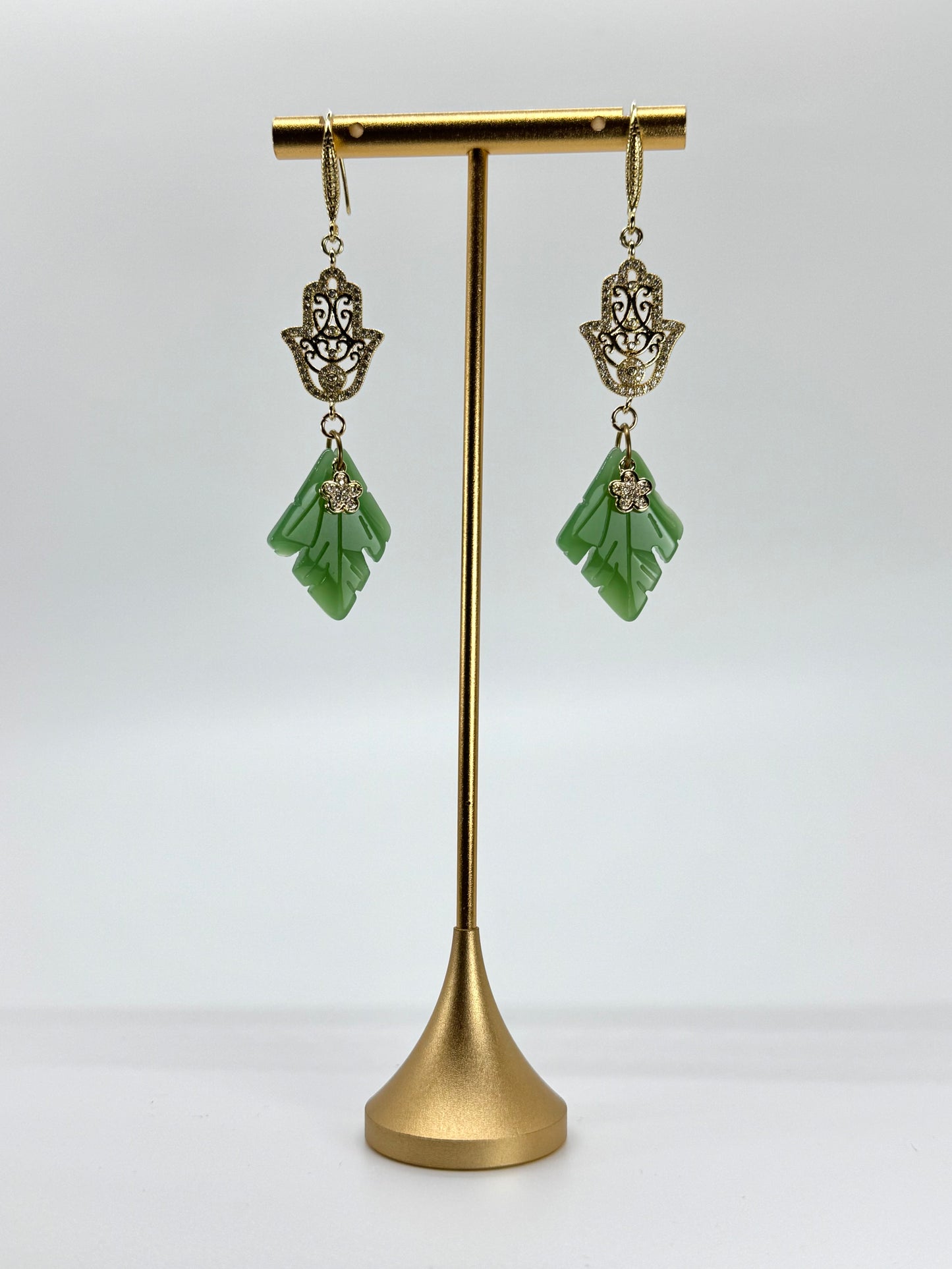Green earrings on a gold stand against a white background