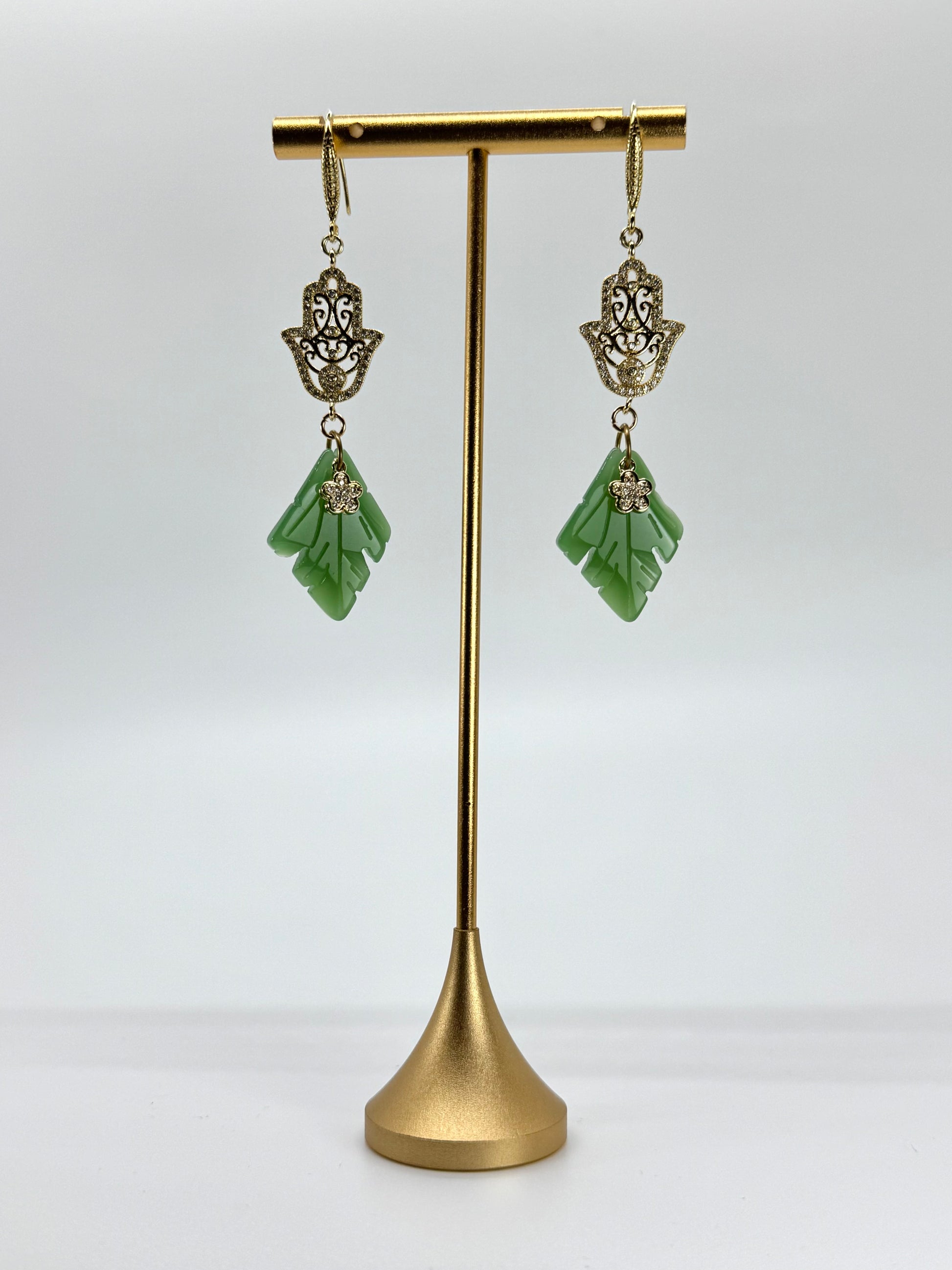 Green earrings on a gold stand against a white background