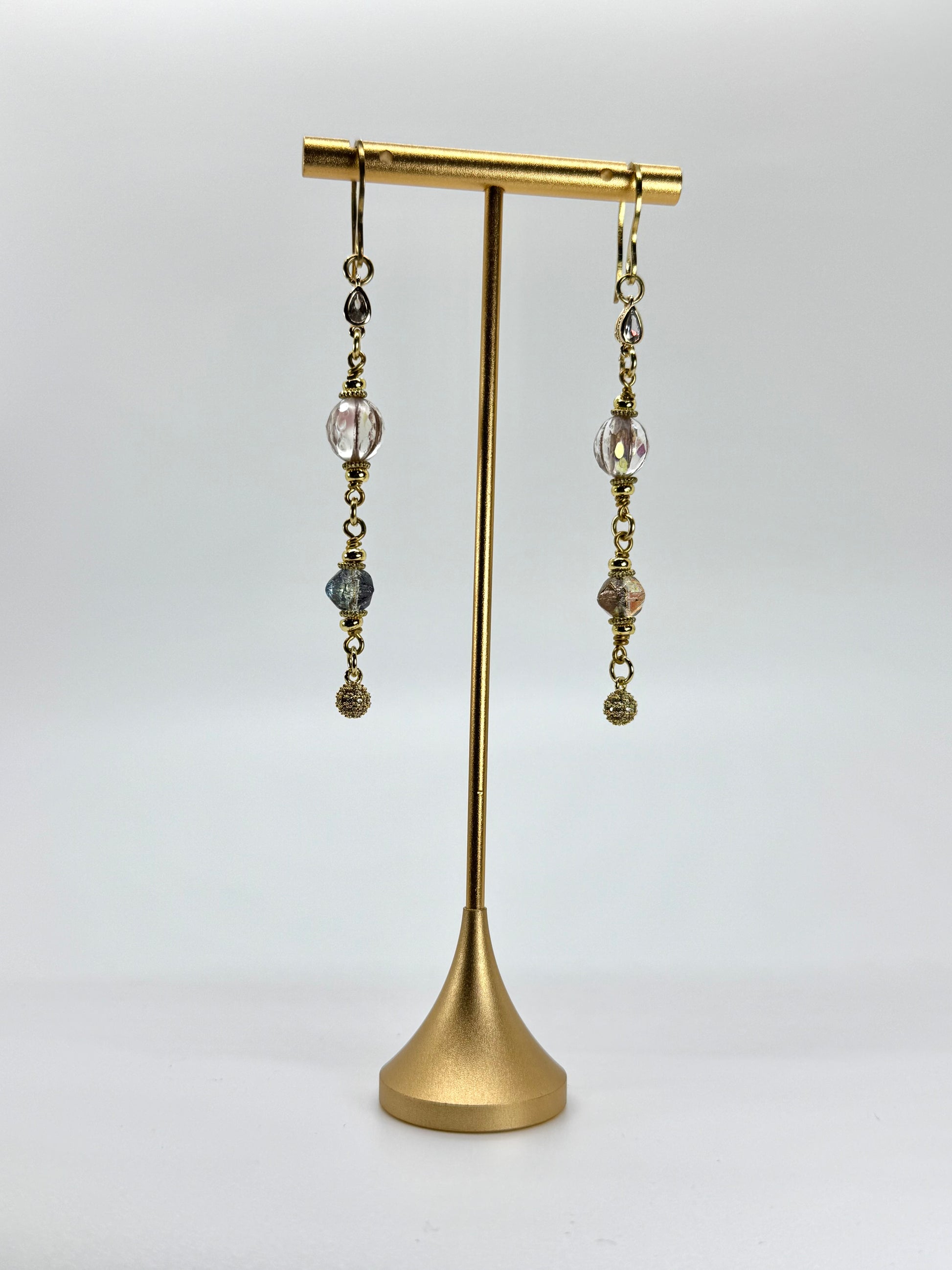 Pair of dangling earrings on a gold stand against a white background