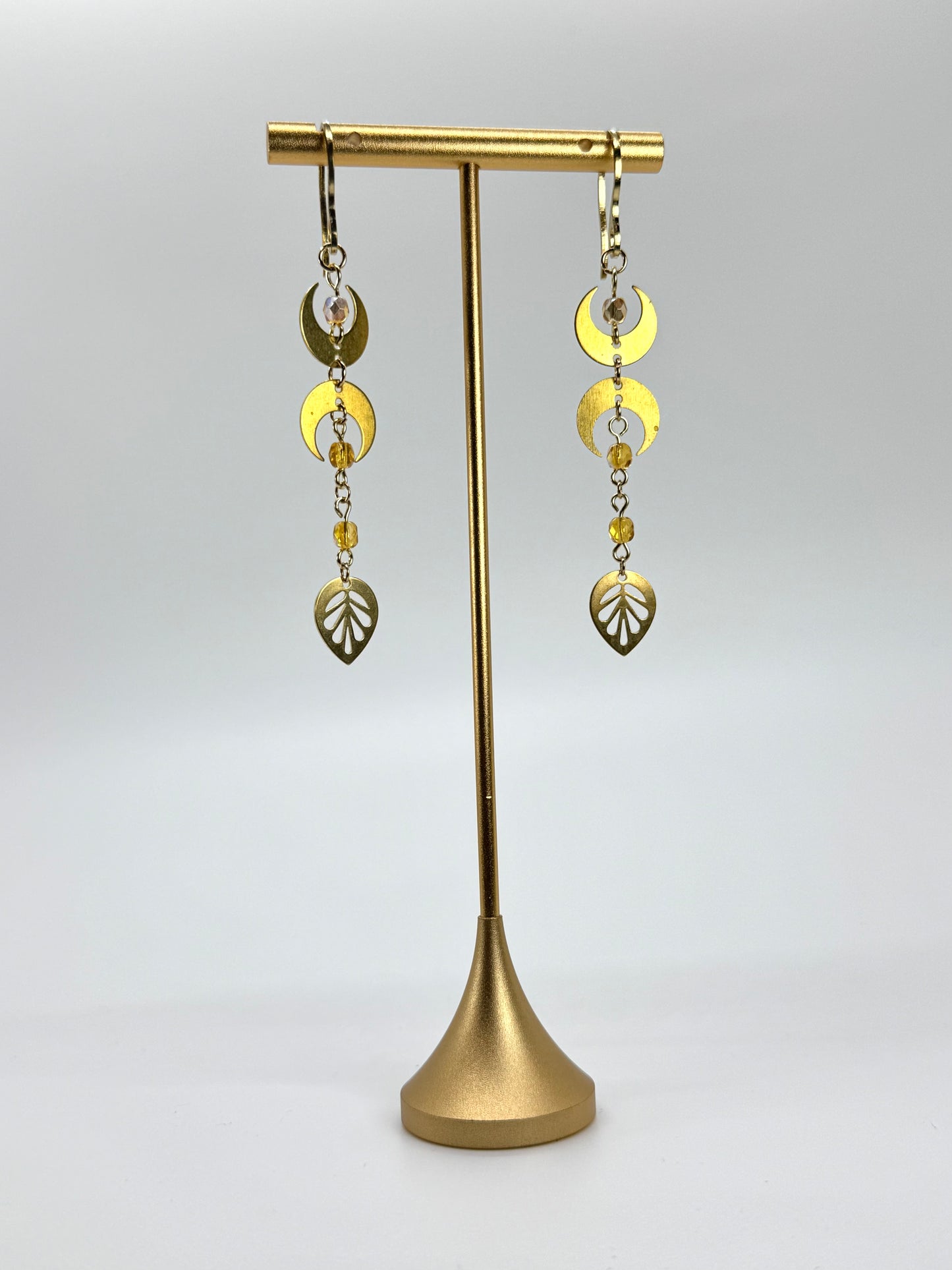 Gold earrings on a gold stand against a white background