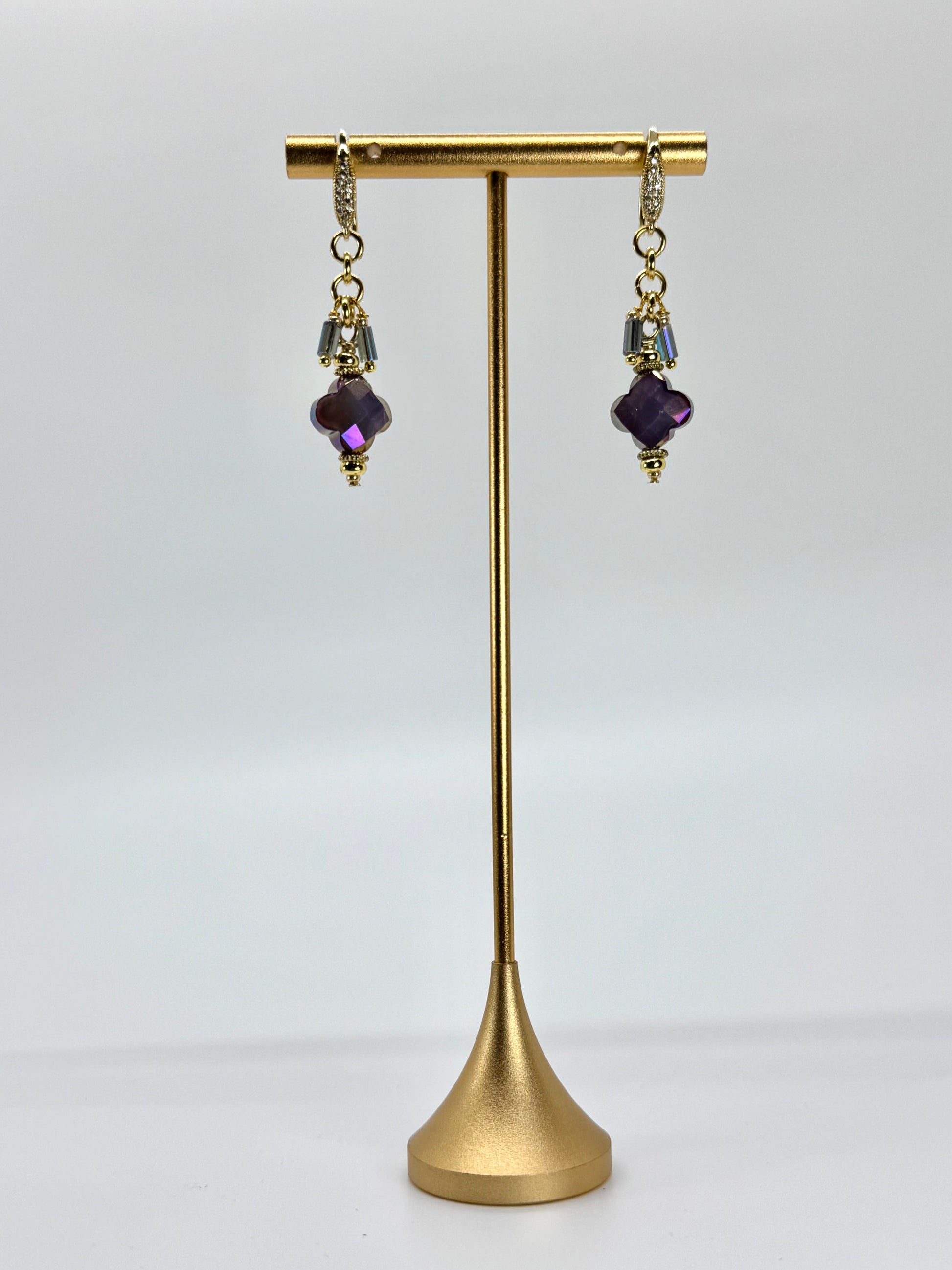 Gold earring stand with purple gemstone earrings on a white background