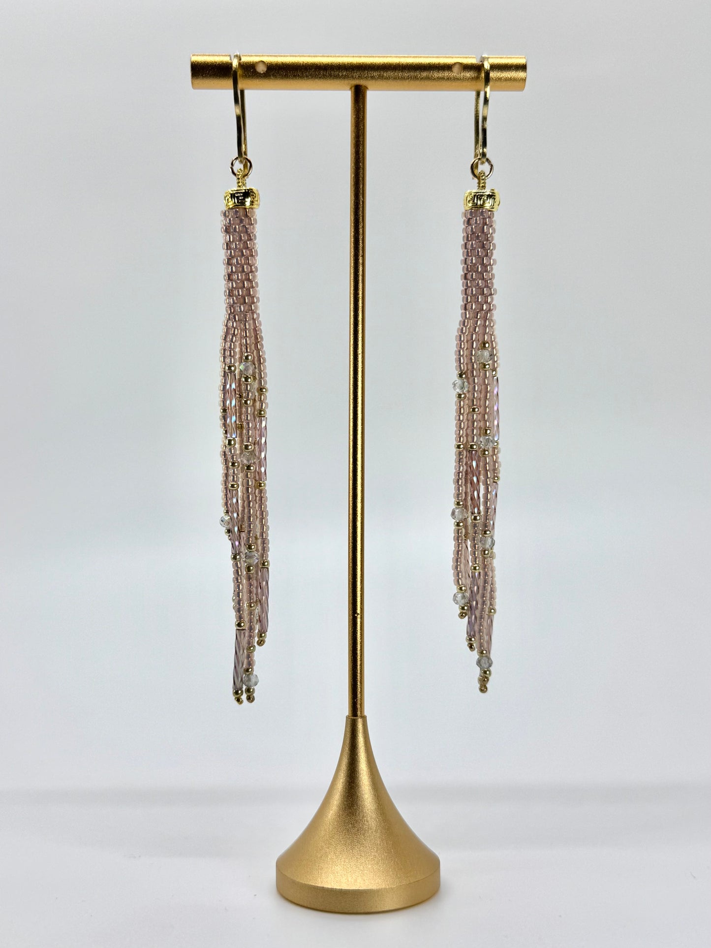 Pair of beaded tassel earrings on a gold stand against a white background