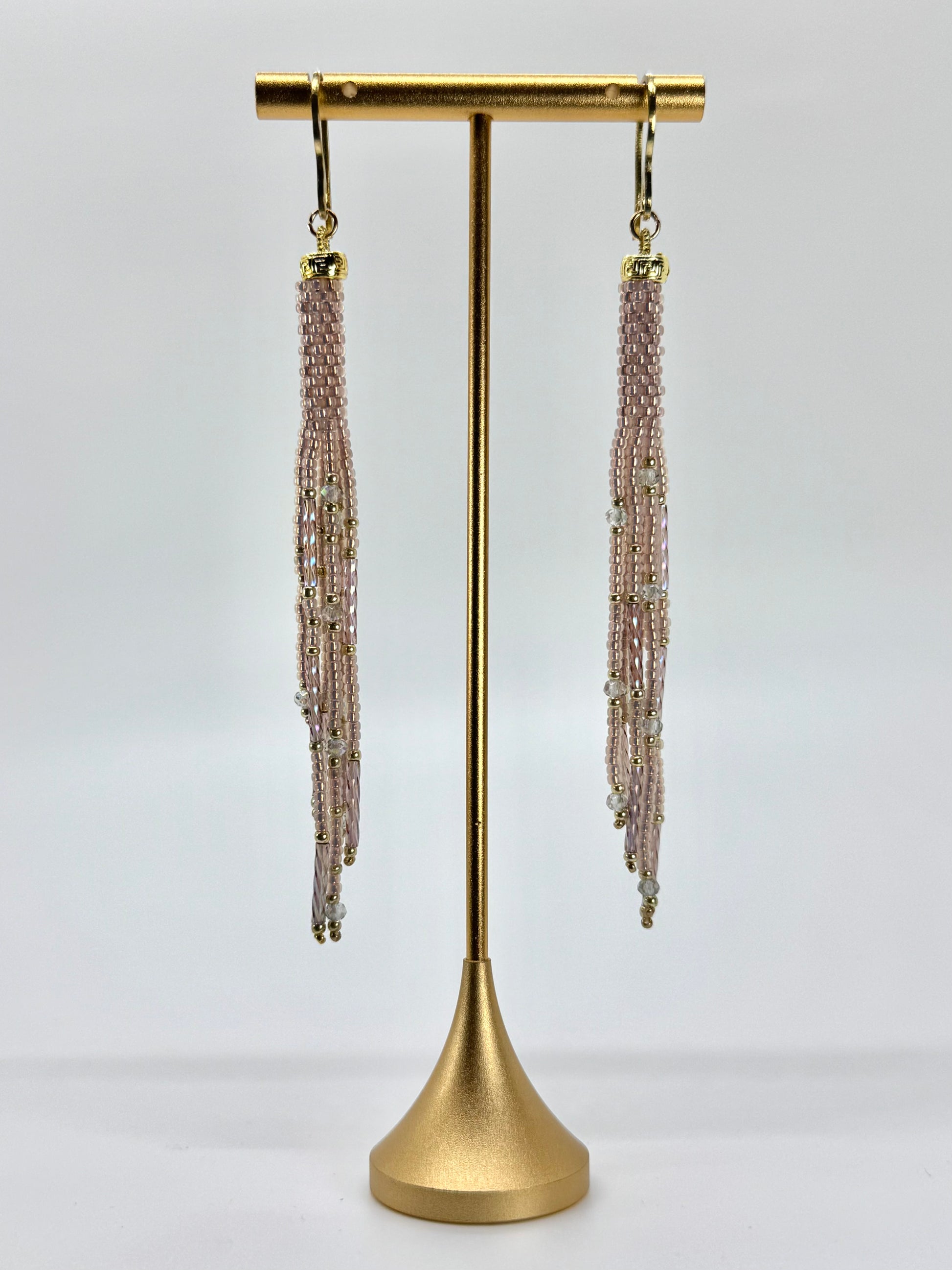 Pair of beaded tassel earrings on a gold stand against a white background