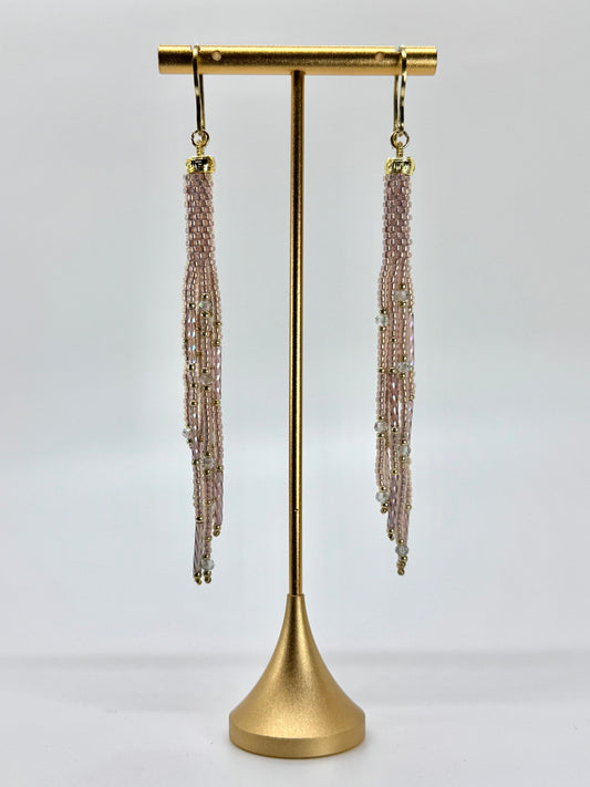 Pair of beaded tassel earrings on a gold stand against a white background