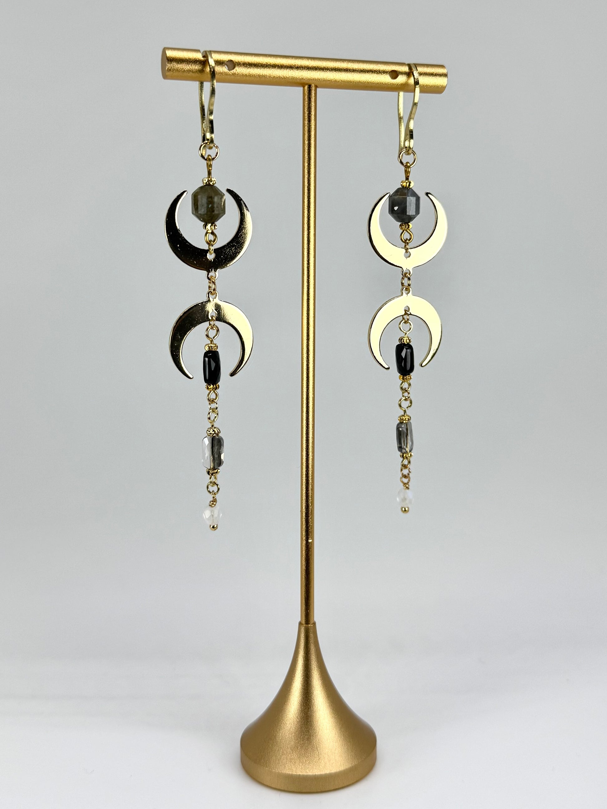 Pair of earrings with gold crescent moon designs on a gold stand against a gray background
